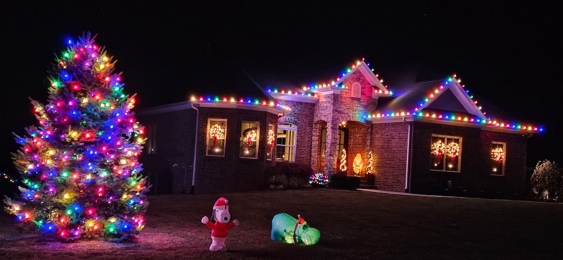 A house decorated with Christmas lights, a lit Christmas tree, and yard decorations like Santa and a dragon.