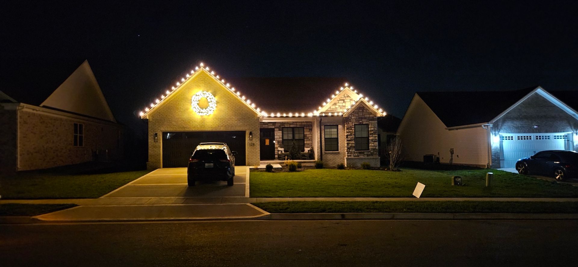 House at night, decorated with Christmas lights, with a car in the driveway.