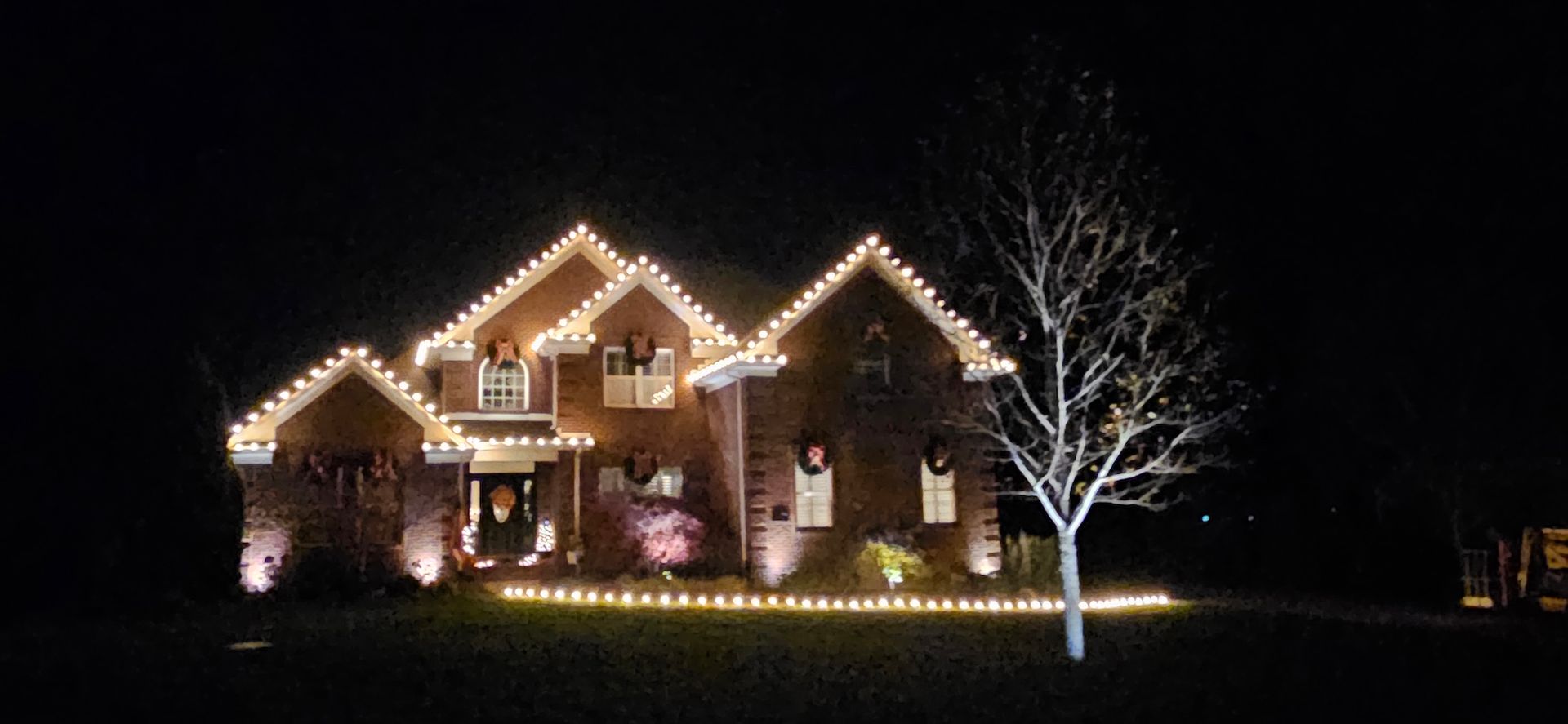 A brick house with Christmas lights at night, a lighted tree to the right.