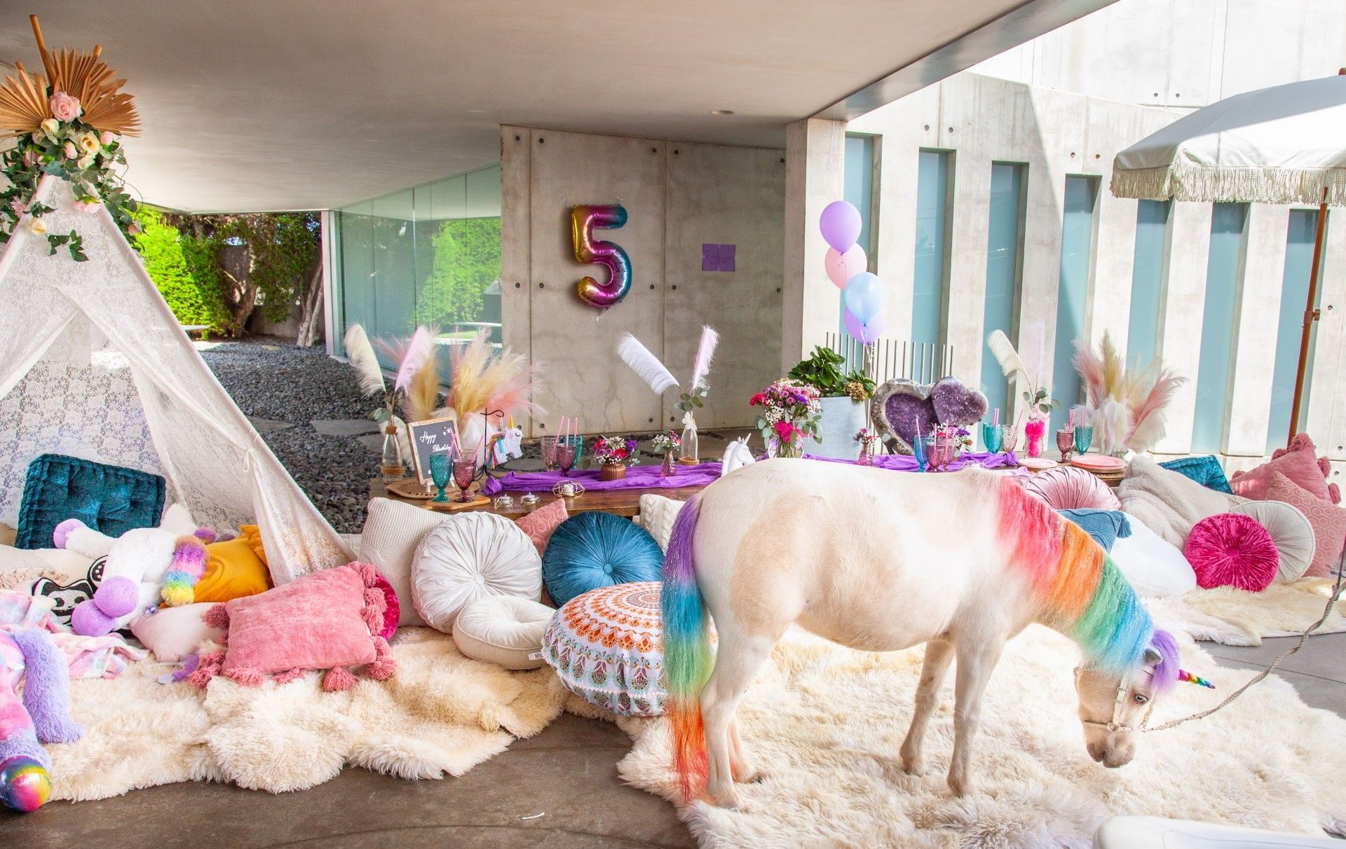 Unicorn-themed party setup with balloons, pastel decorations, and a white horse statue on fluffy white rugs