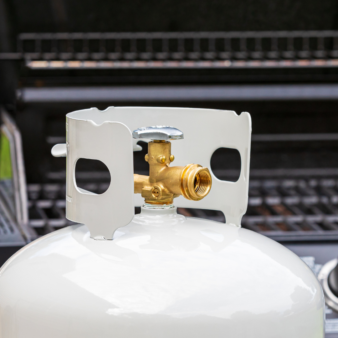 White propane tank with brass valve, next to a grill.