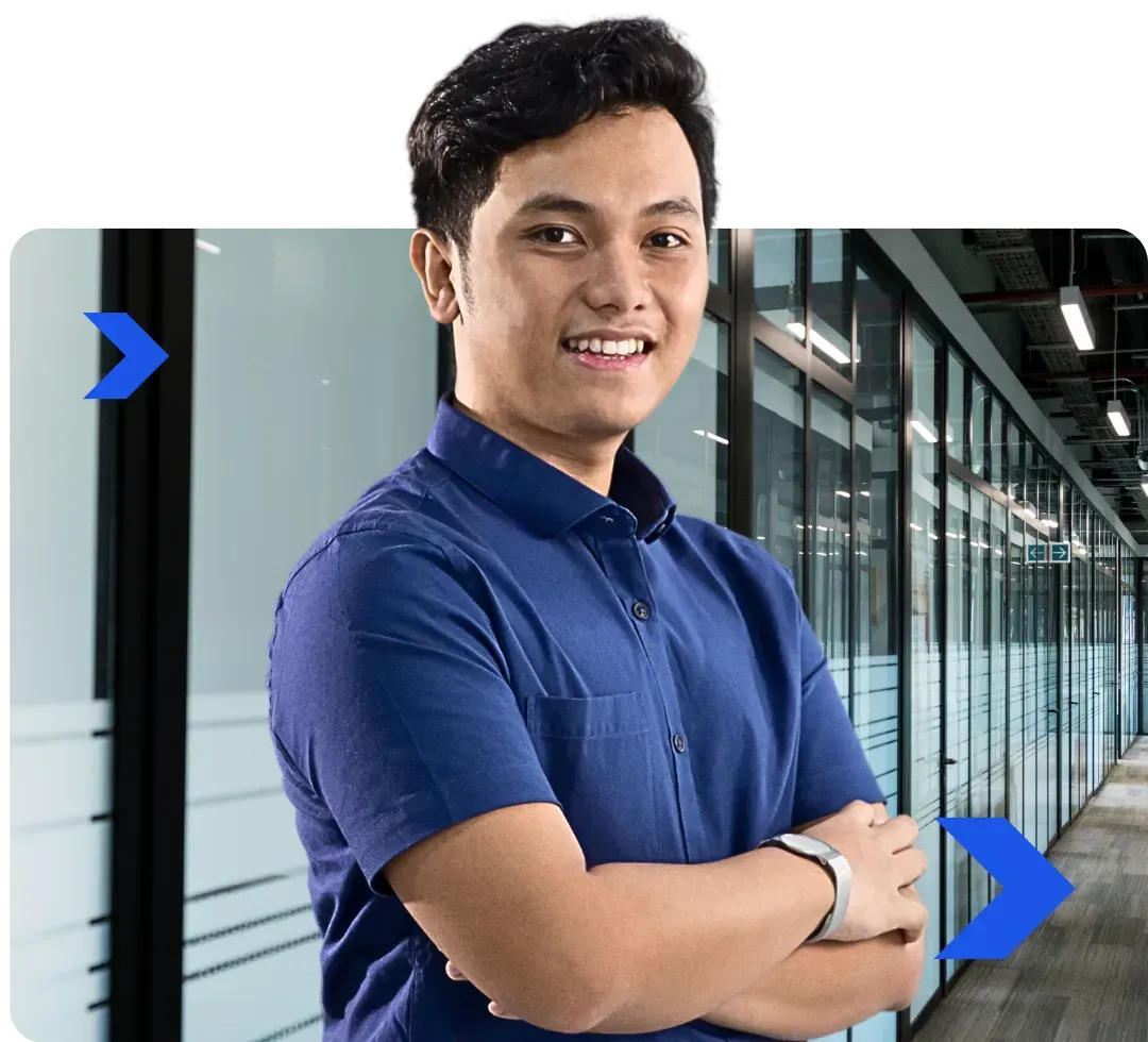 A man in a blue shirt is standing in a hallway with his arms crossed.