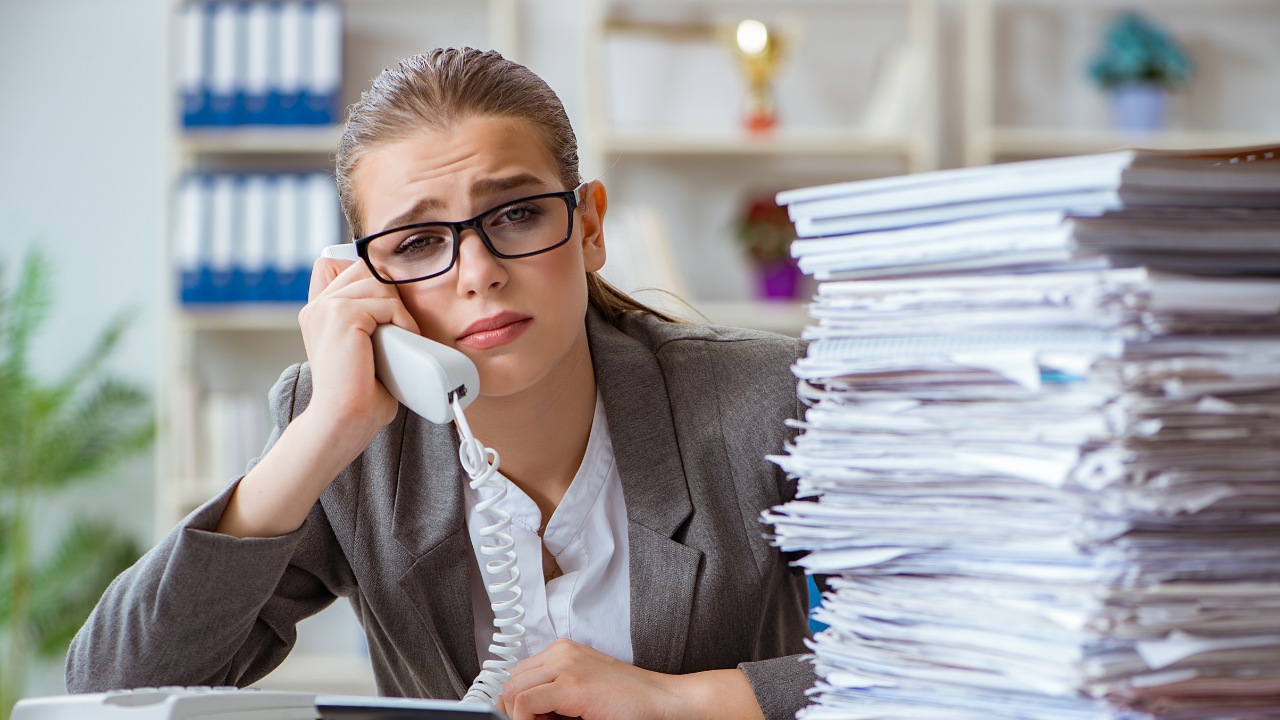 A woman is talking on a phone in front of a pile of papers.