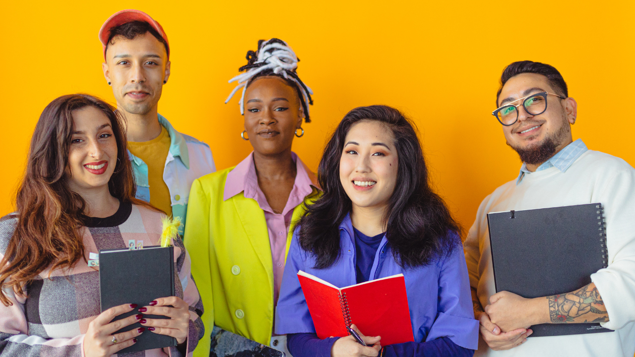 A group of young people are standing next to each other holding notebooks.