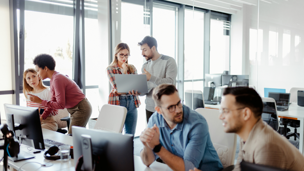 A group of people are standing around a computer in an office.