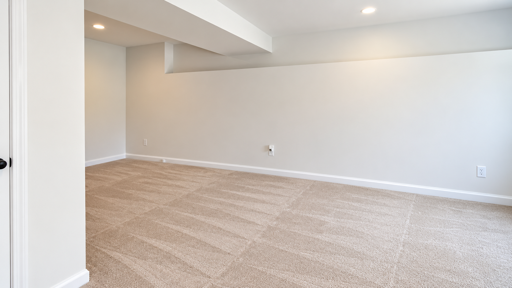 Empty beige-carpeted living room with white walls and ceiling beam