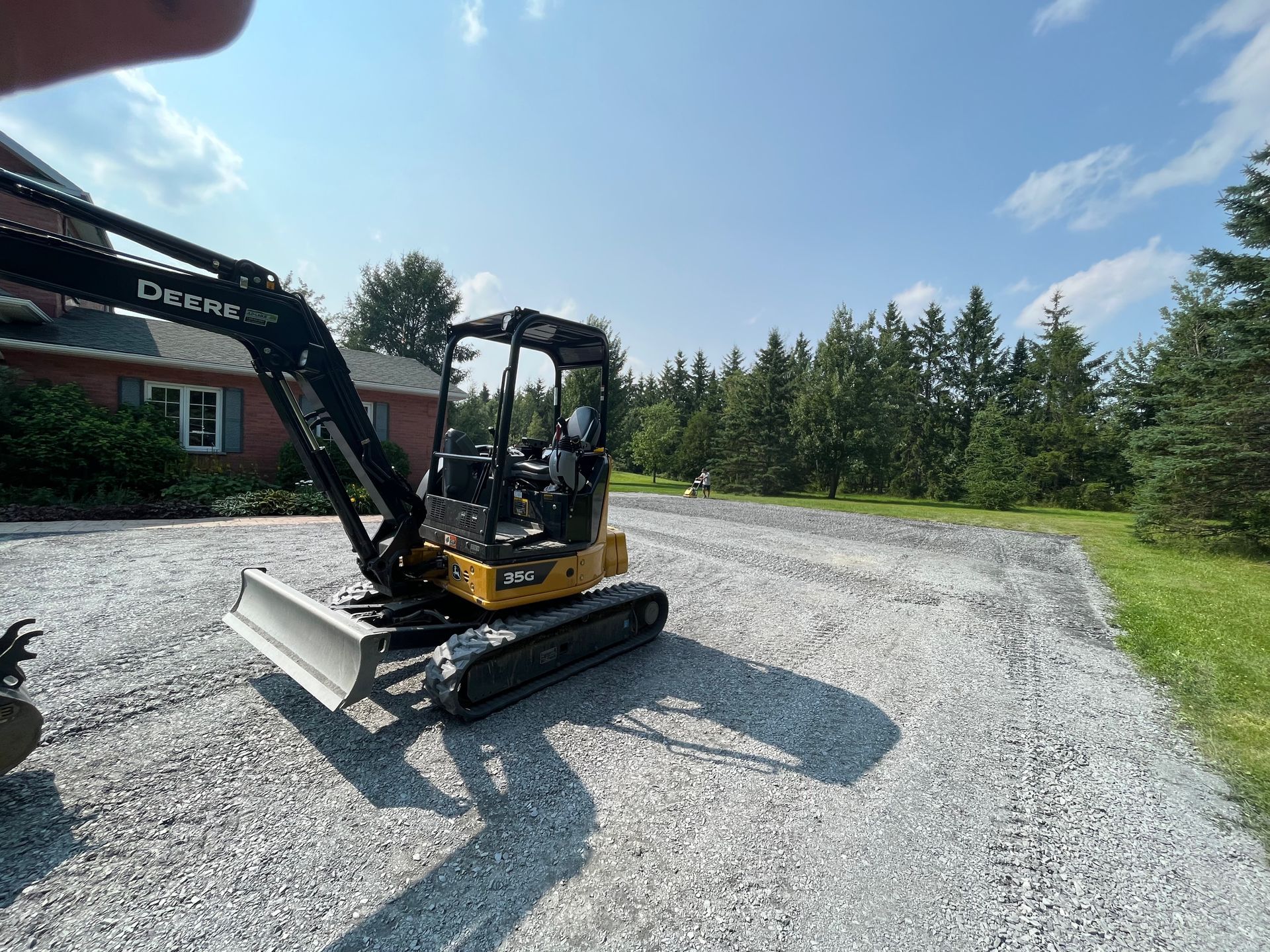 Une petite excavatrice est garée sur un chemin de gravier devant une maison.