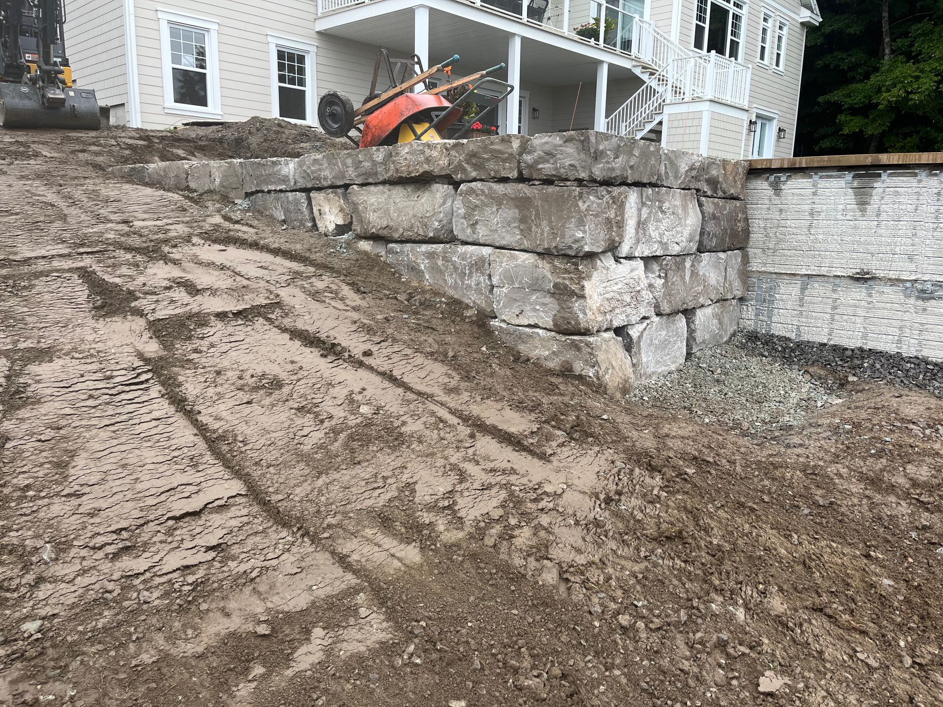 Un grand mur de pierre est en train d'être construit devant une maison.