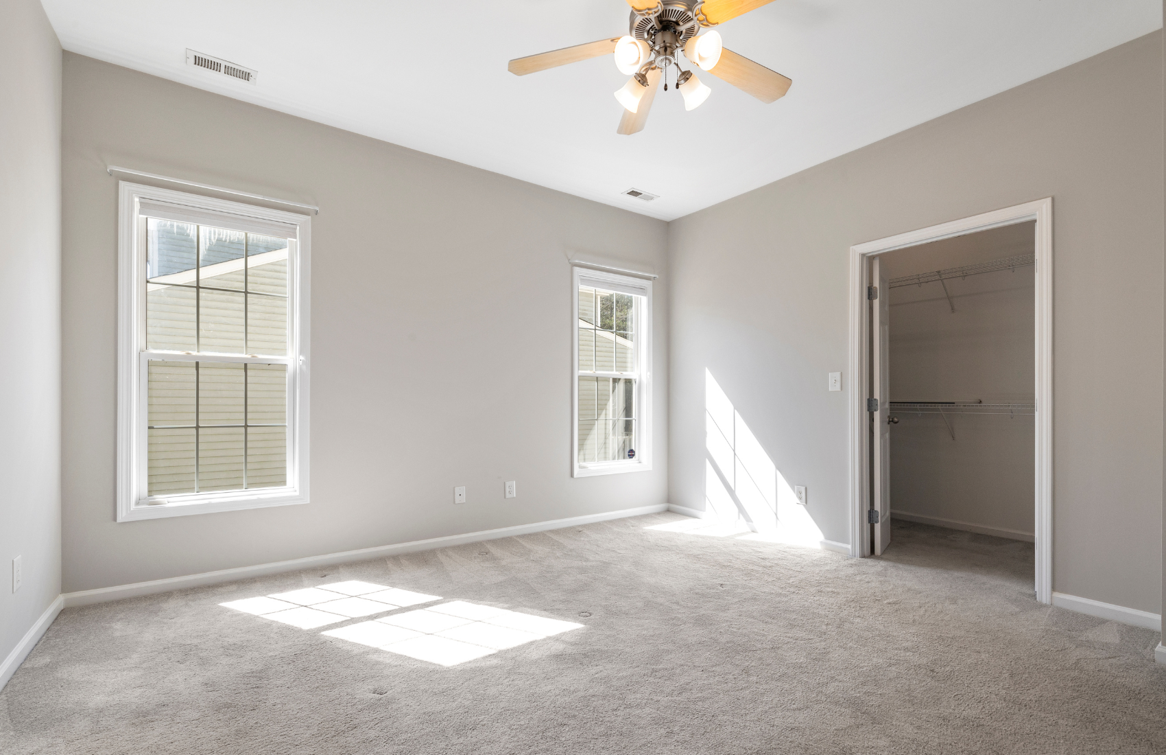 An empty bedroom with a ceiling fan and two windows.