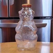 Clear glass bear-shaped honey bottle with a gold cap on a wooden table.