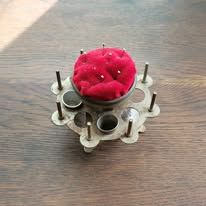 Vintage metal sewing tool with red pincushion, holds needles and small tools.