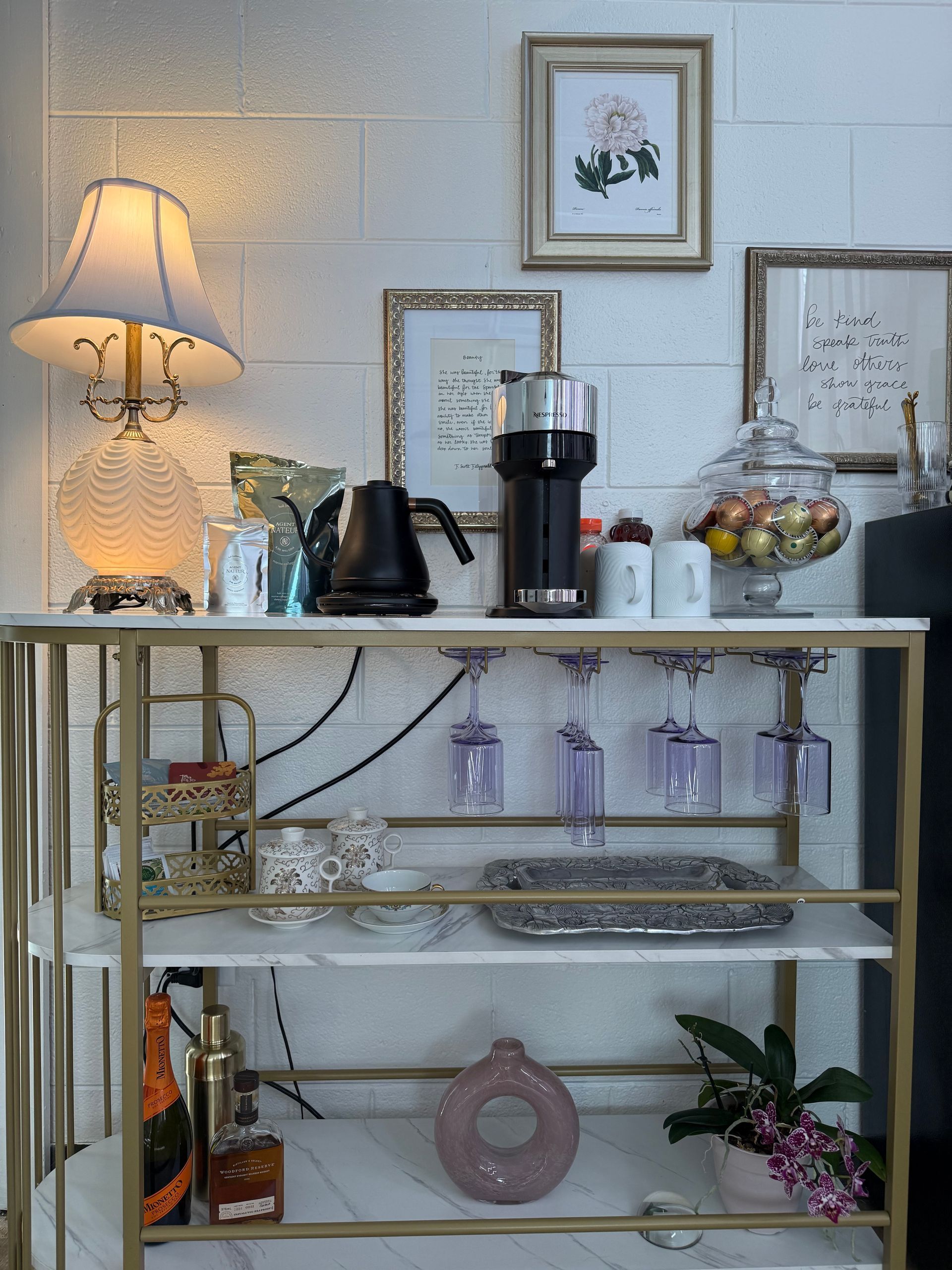 Decorative home bar cart with lamp, coffee maker, glassware, wine bottle, and flowers