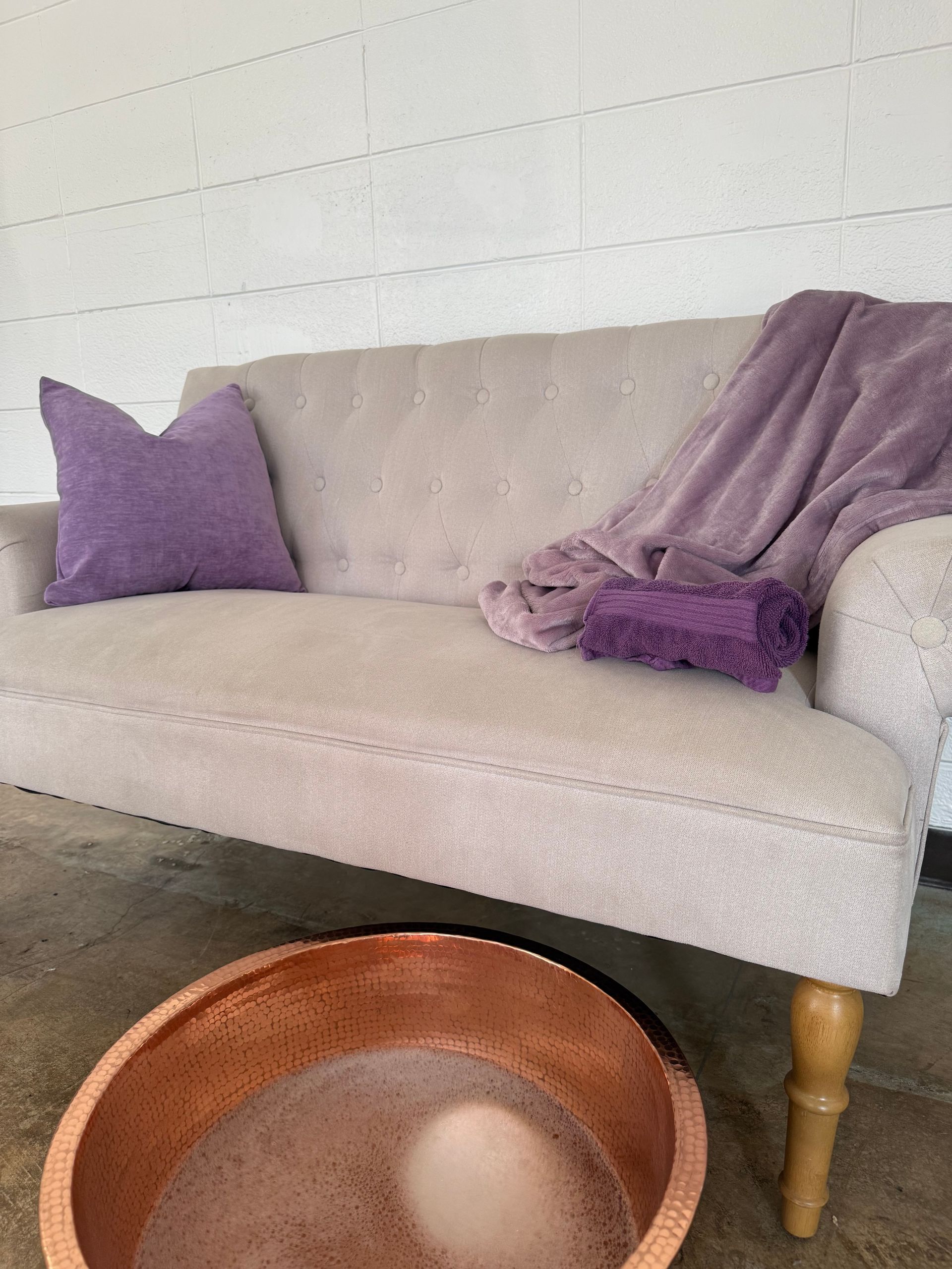Light beige sofa with purple pillows and throw blanket beside a copper bowl on the floor