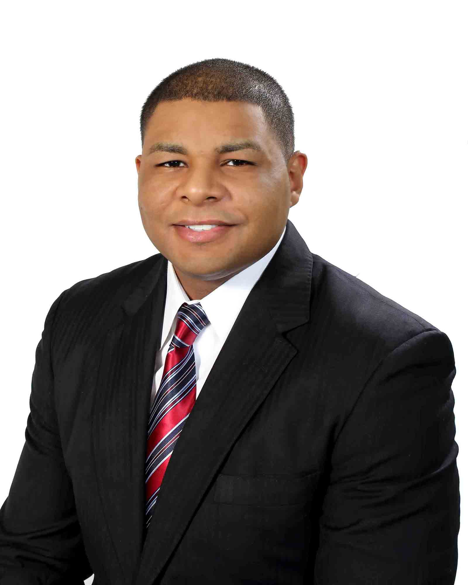 Portrait of a man in a black suit, white shirt, and red striped tie against a white background