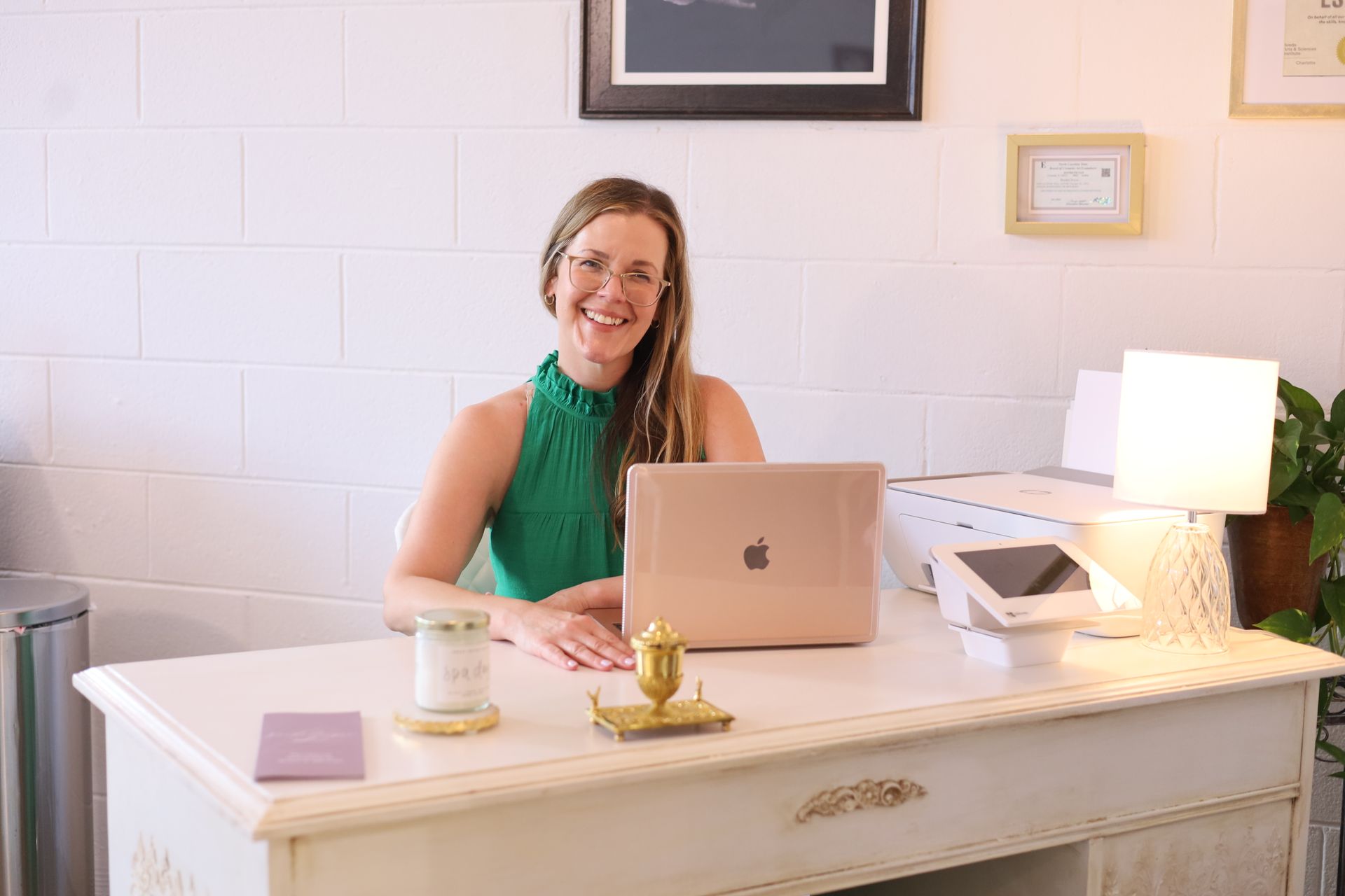 Smiling person seated at a desk with a laptop in a bright office