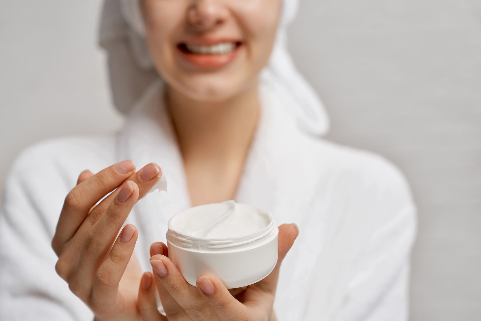 A woman in a bathrobe is holding a jar of cream in her hands. 