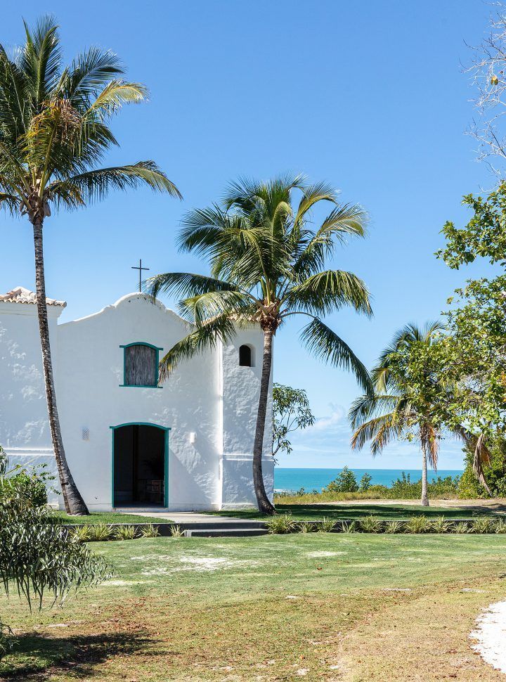 Uma pequena igreja branca com palmeiras na frentePousada Quadradinho de Trancoso
