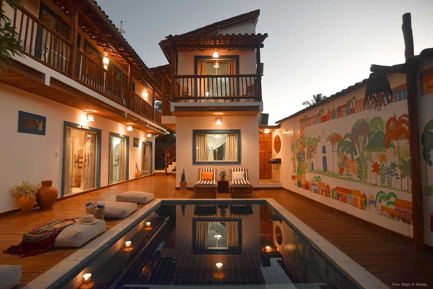 Pátio com piscina, edifícios iluminados e mural. Ambiente noturno.