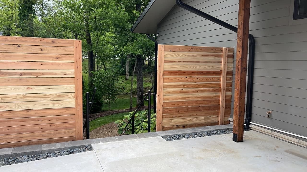 Wooden fence and gate beside apartment buildings, with stairs and a dirt path in a courtyard.