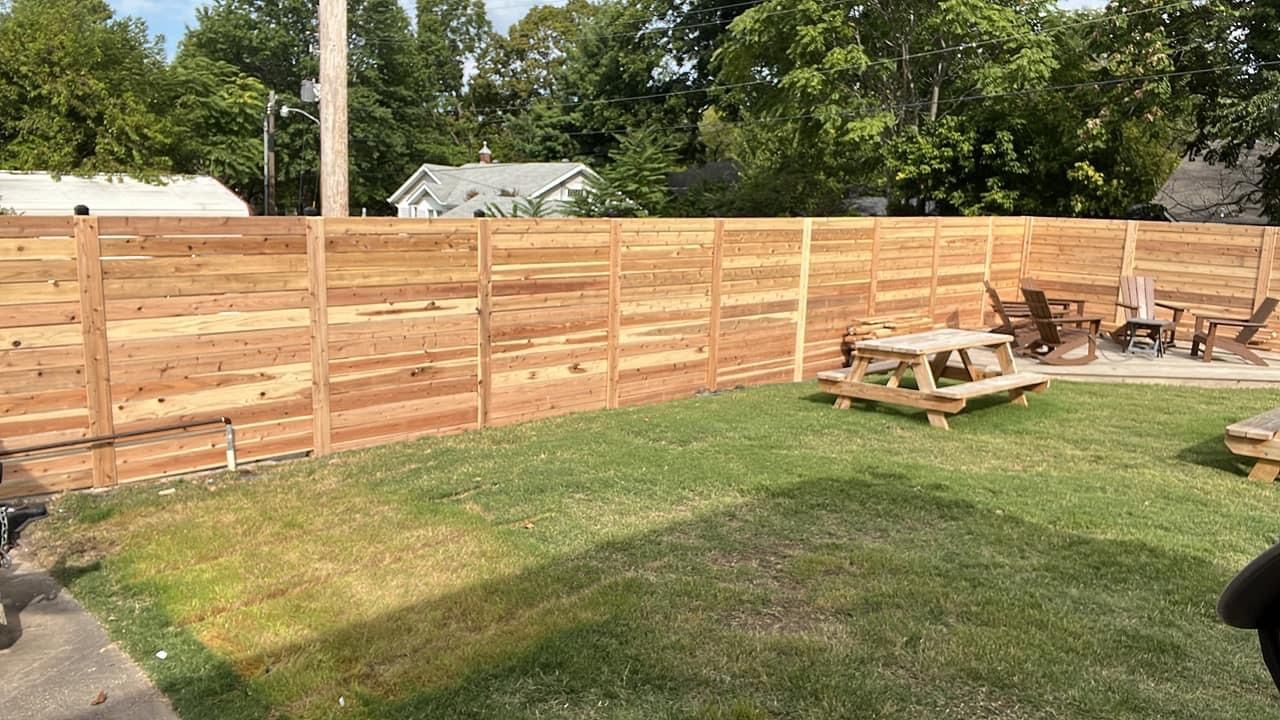 Wooden privacy fence enclosing a grassy yard with picnic tables and trees in the background