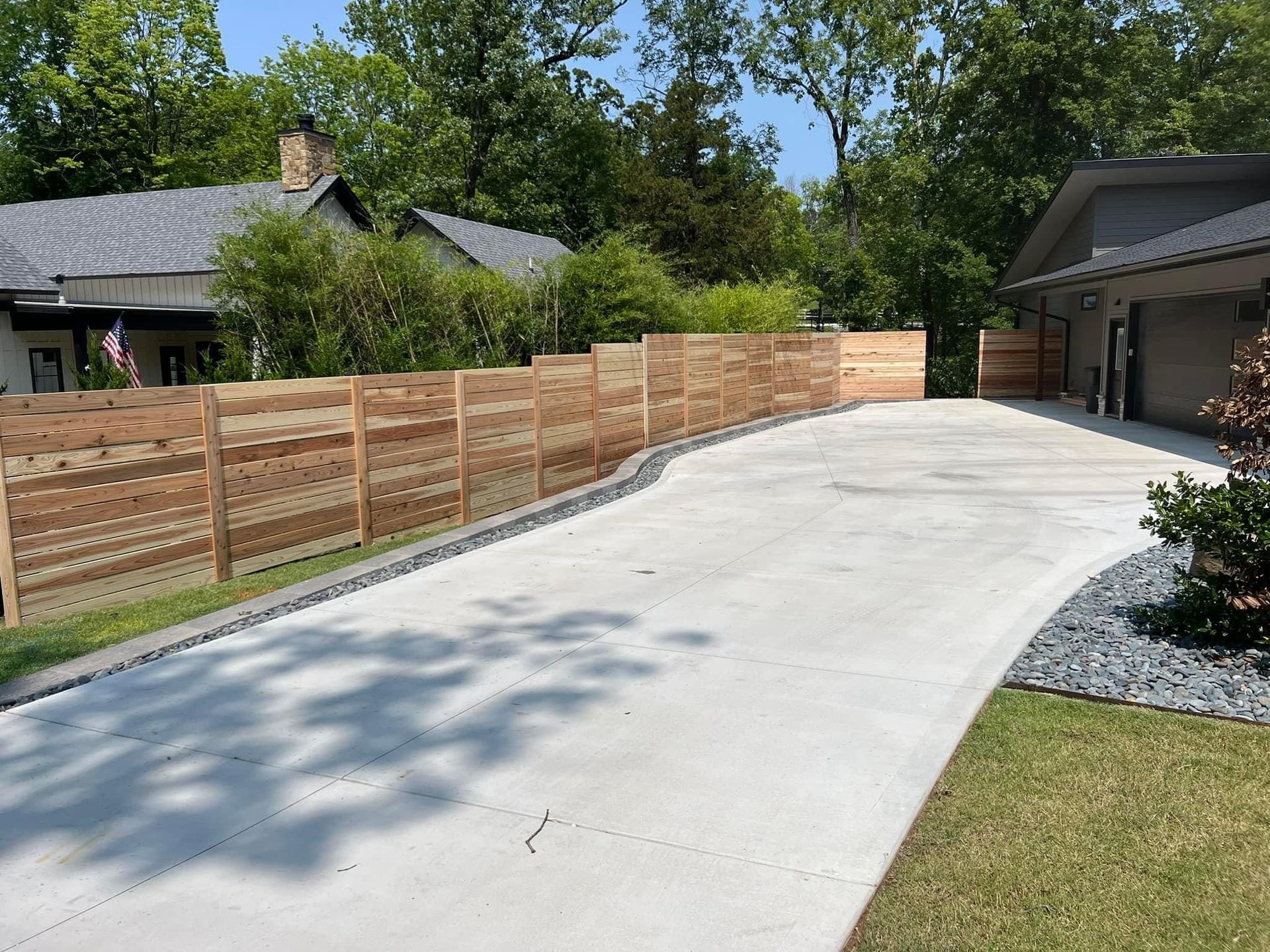 Curved concrete driveway beside a wooden fence and garage, with trees and lawn in a suburban yard