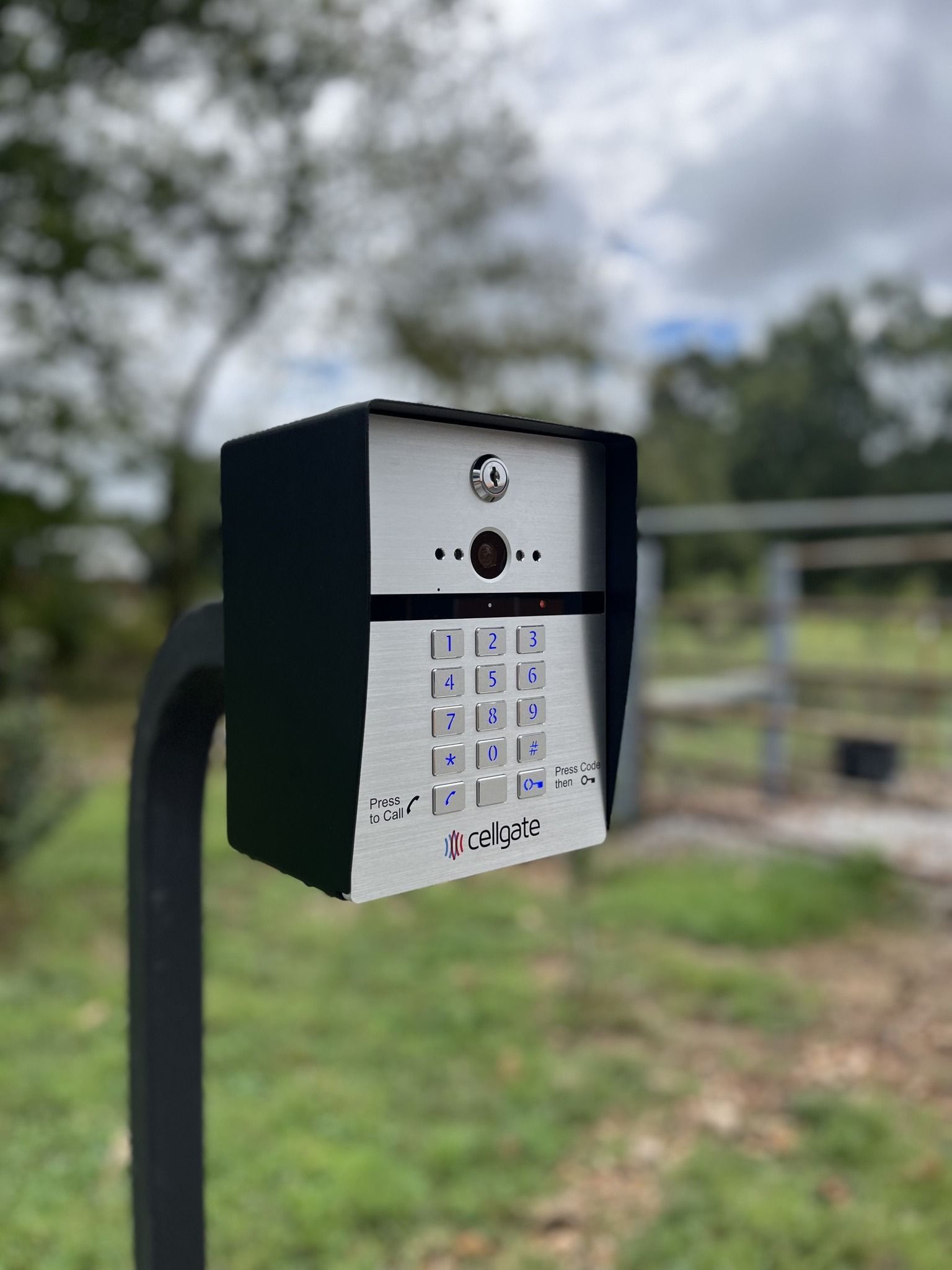 Black outdoor keypad access box mounted on a post, with blurred park background