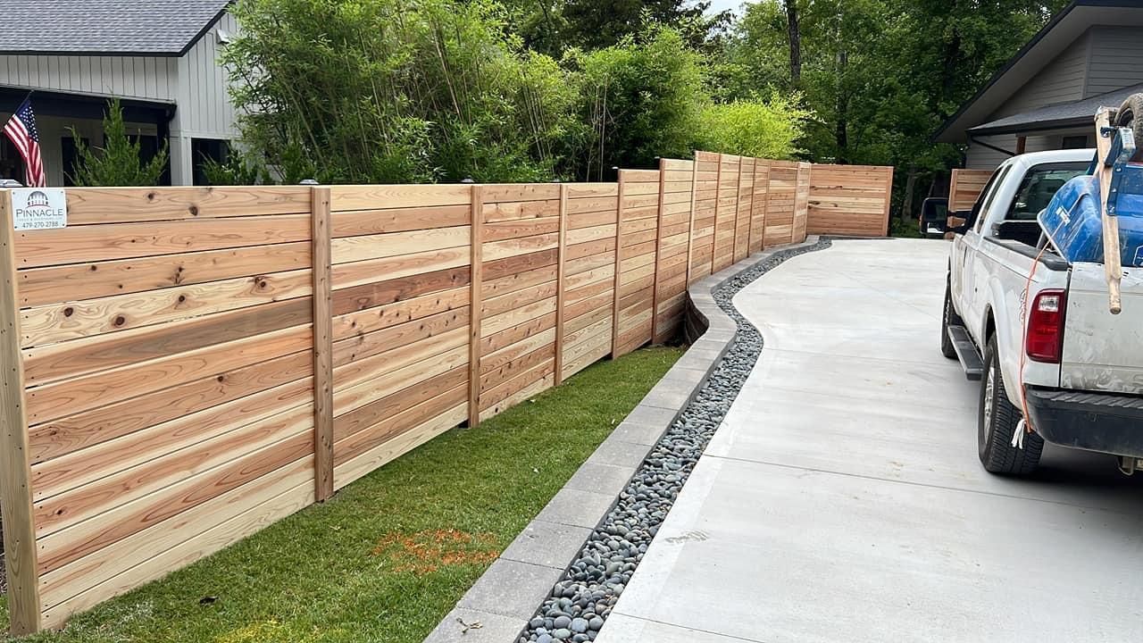 Wooden fence along a curved concrete driveway beside a parked white pickup truck.