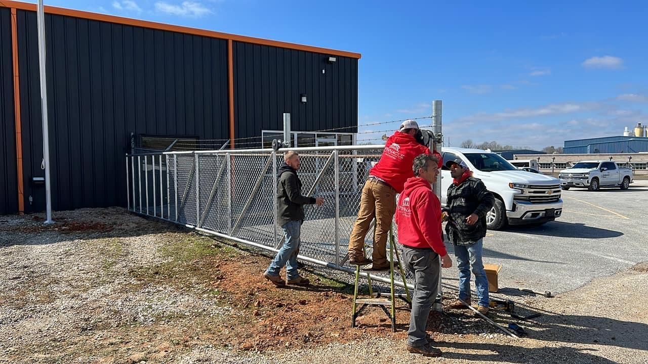 Workers loading materials into a truck beside a dark building on a gravel lot under a blue sky