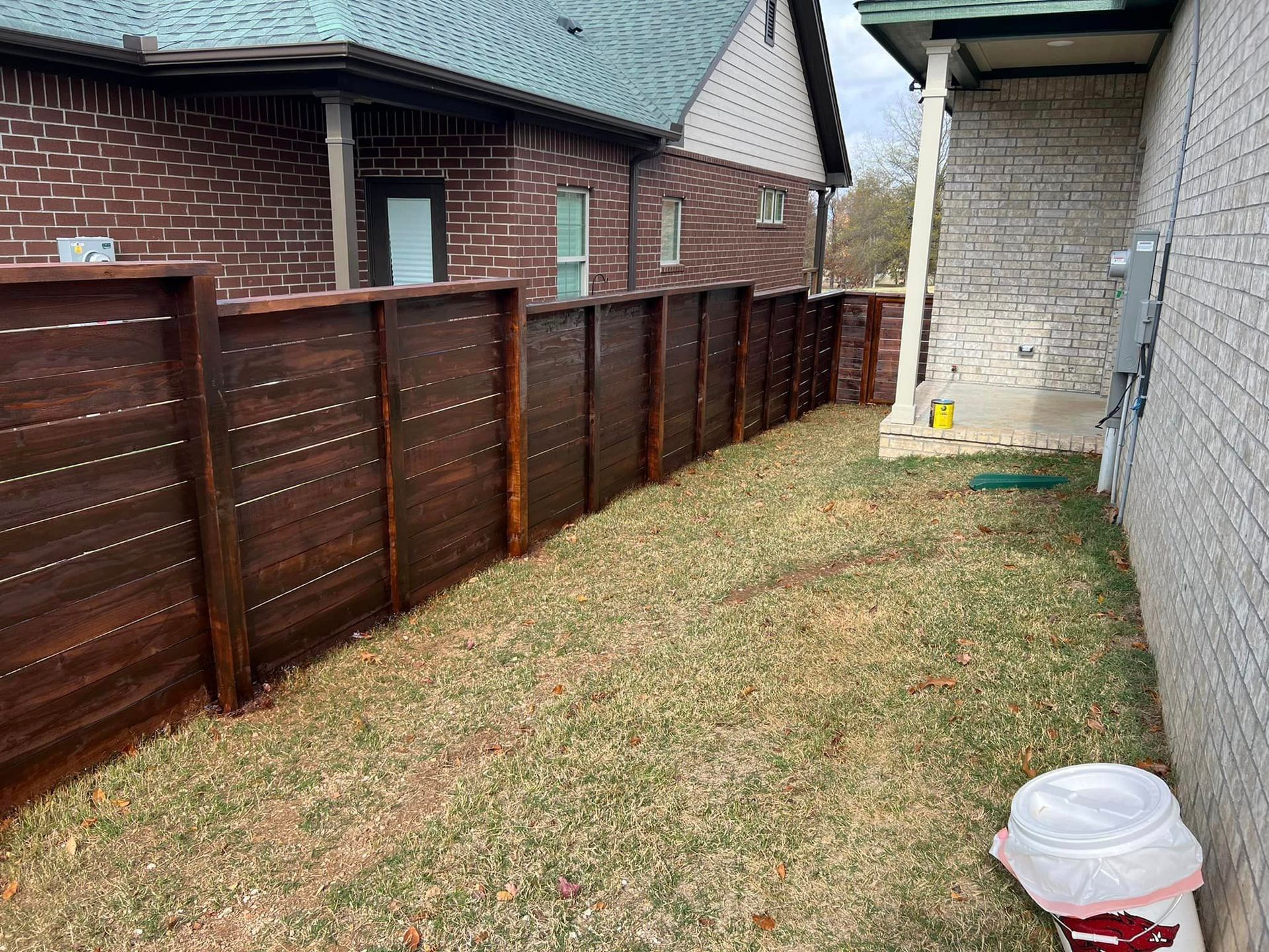Narrow backyard with brown wooden fence, brick houses, and a small covered patio area