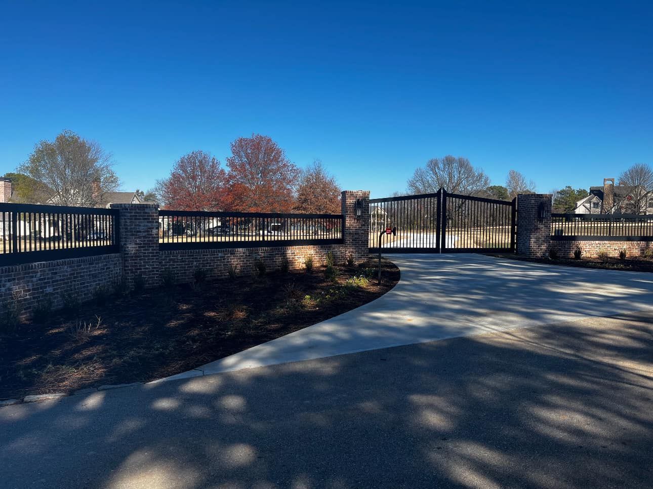 Black metal gate and fence along a curving paved path under a clear blue sky