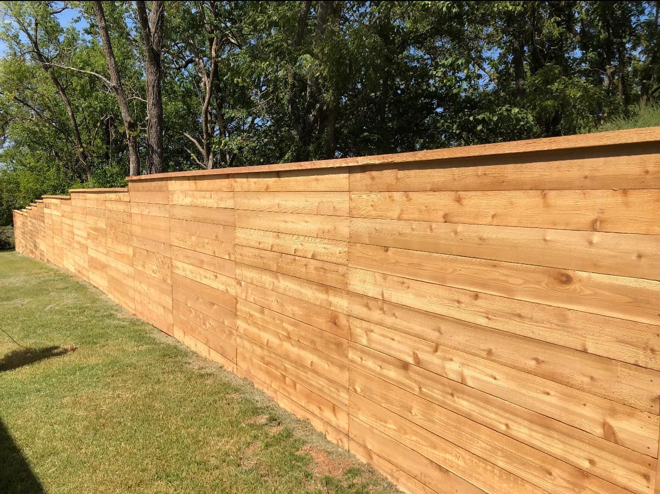 Long wooden privacy fence along a grassy yard with trees in the background