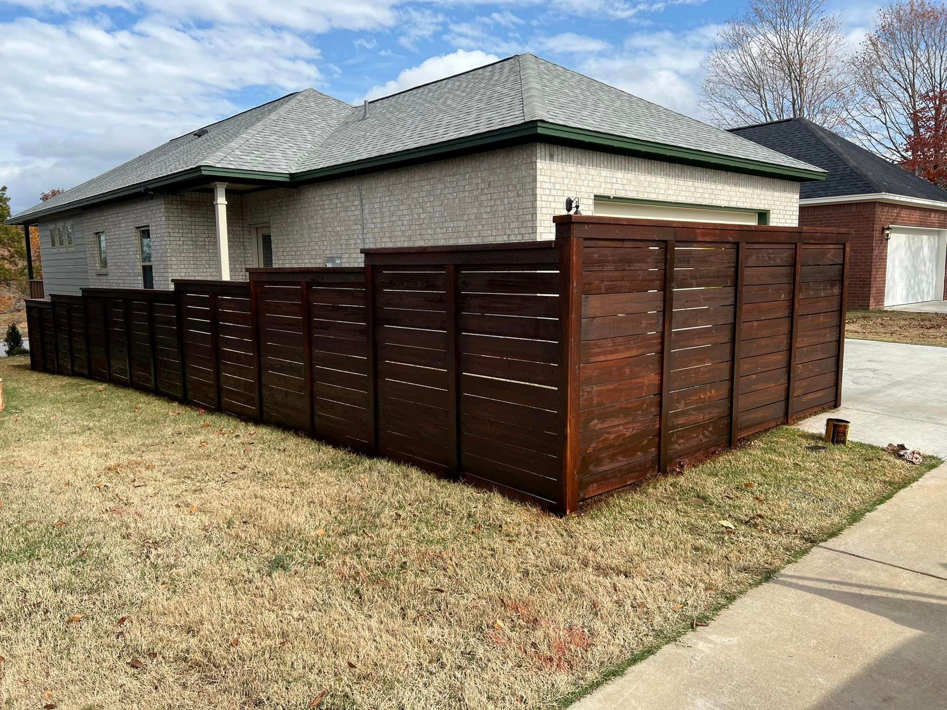 Brown wooden privacy fence around a suburban corner lot beside a brick house and sidewalk