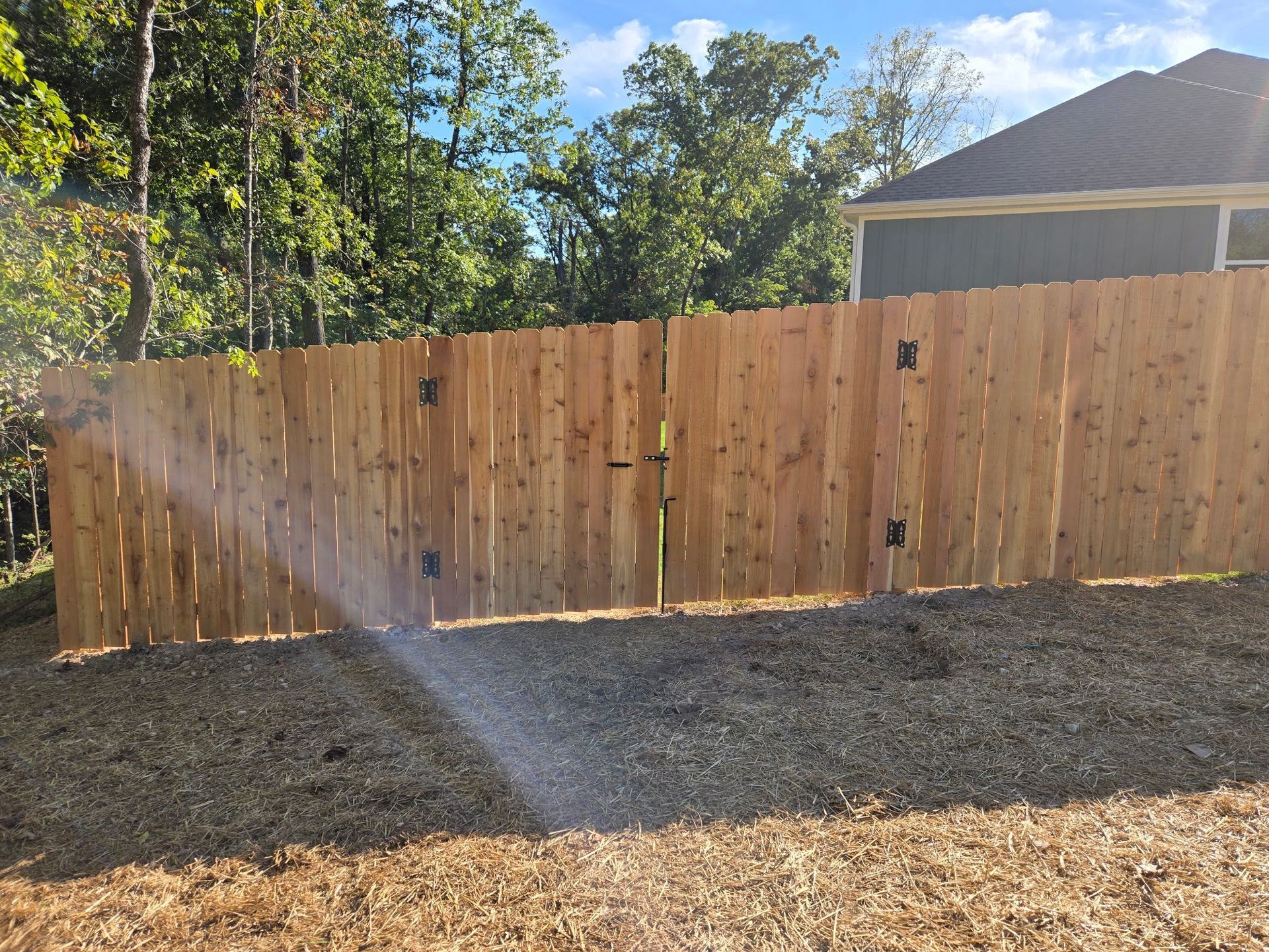 Wooden fence behind gravel yard with a sprinkler spraying water in sunlight