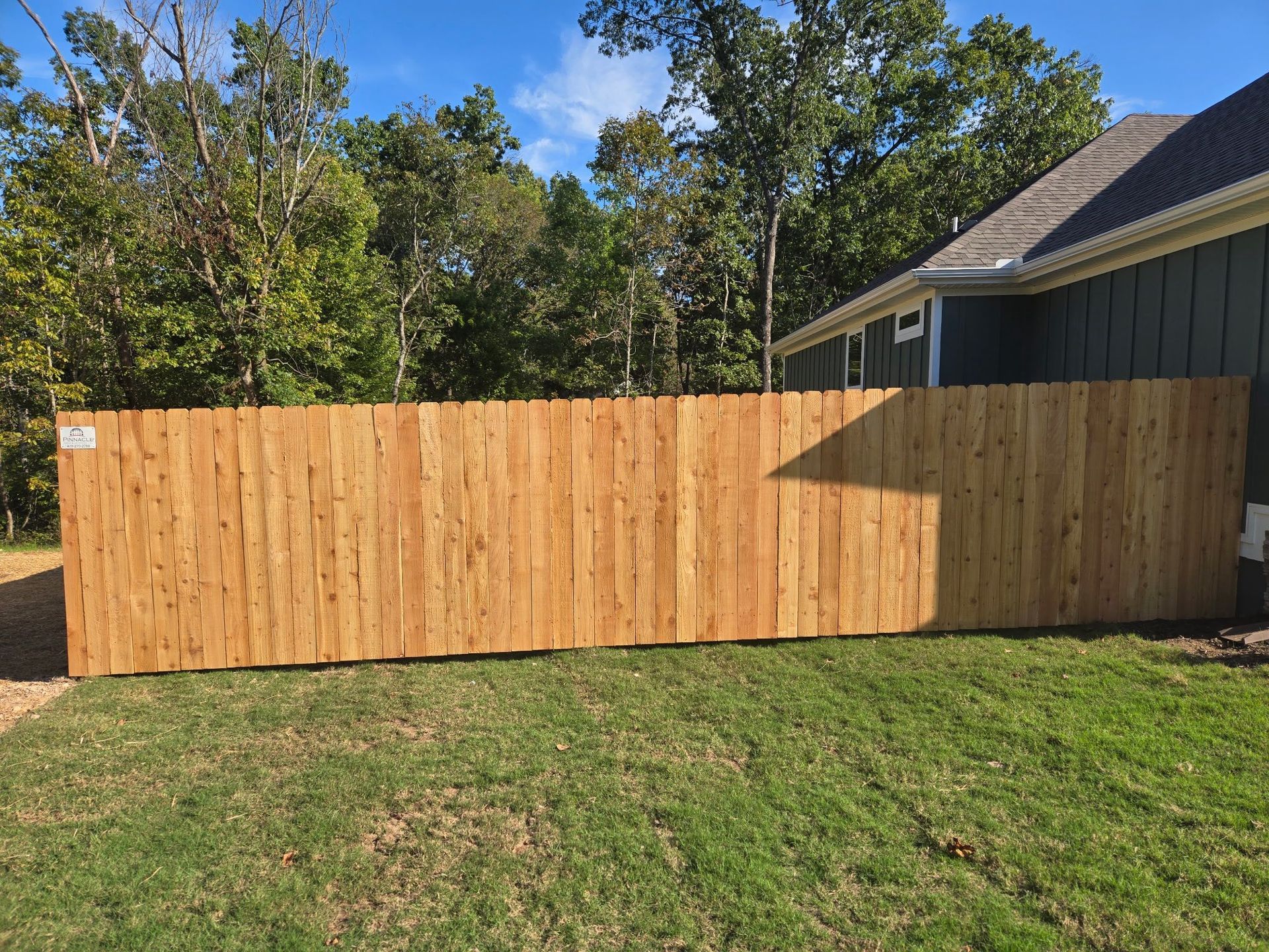 New wooden privacy fence along a grassy yard beside a house, with trees in the background