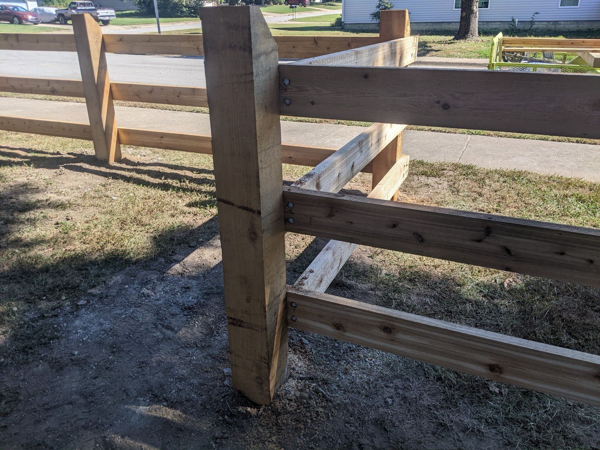 Wooden split-rail fence corner beside a grassy path on a sunny day
