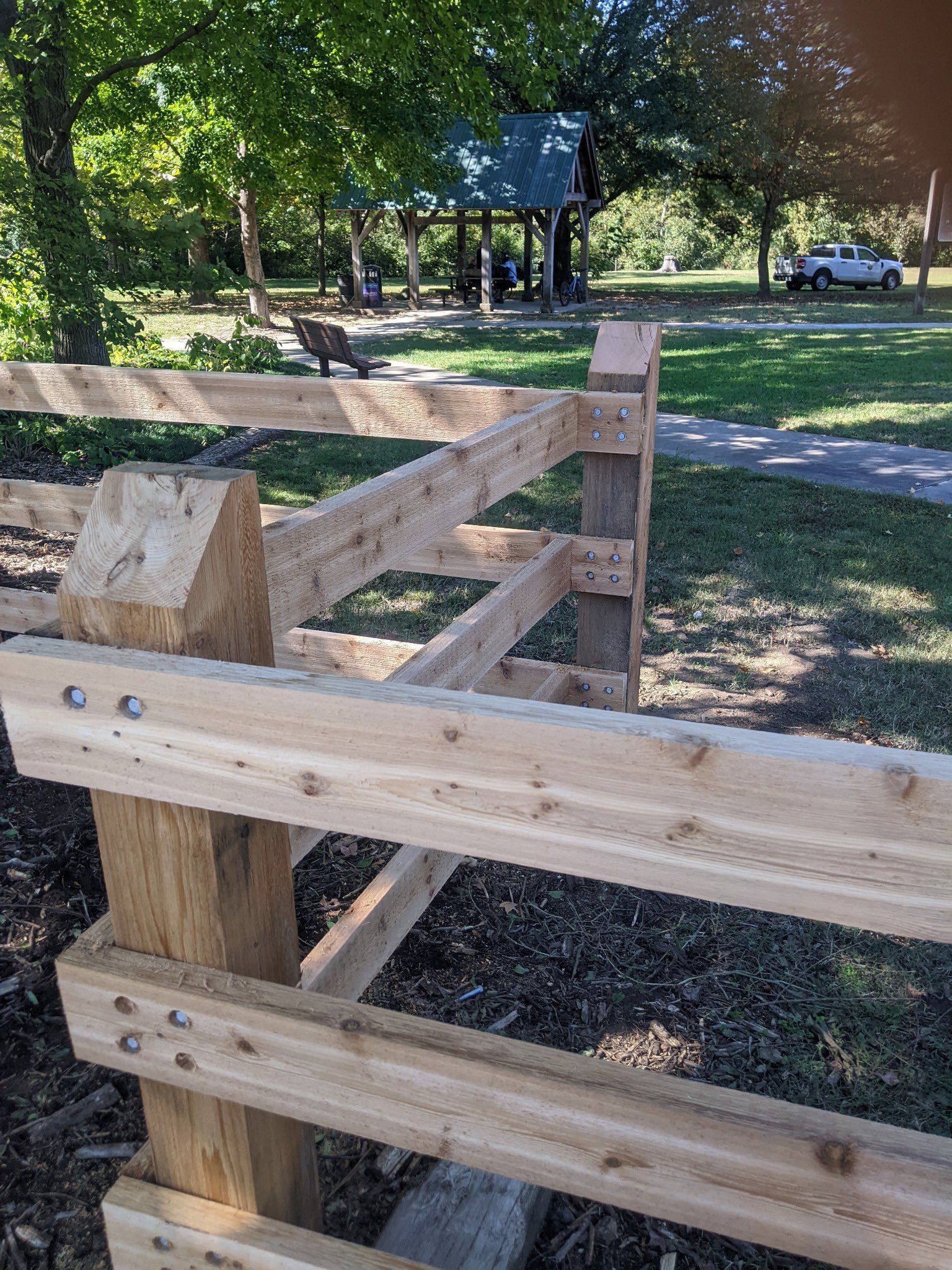 Wooden beam structure in a sunny park with trees and grass in the background