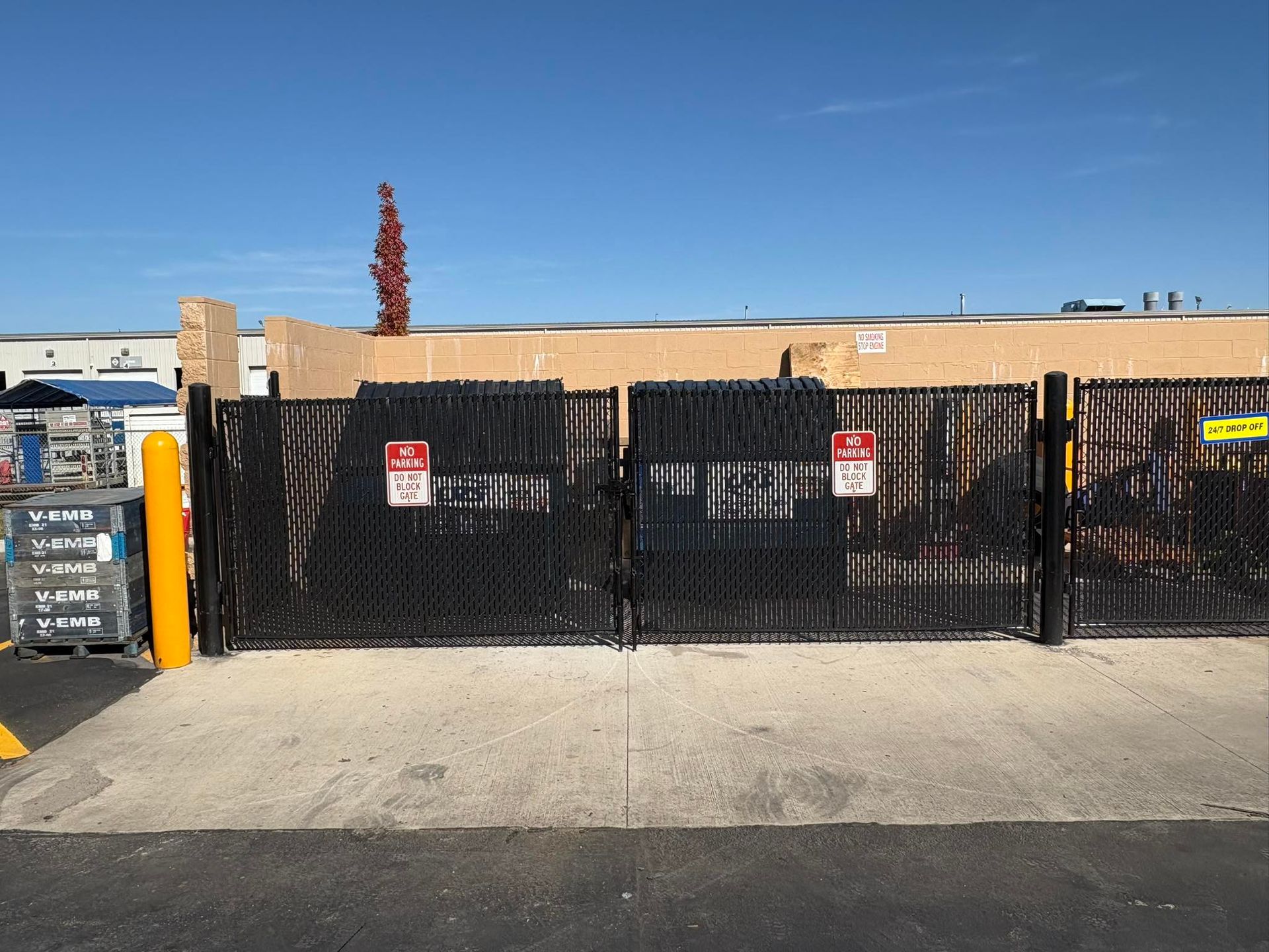 Black chain-link fence and industrial storefront under a clear blue sky