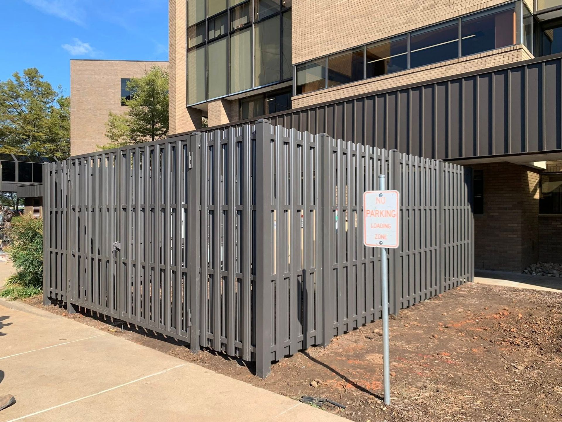 Gray fenced enclosure beside a building with a no-smoking sign in front