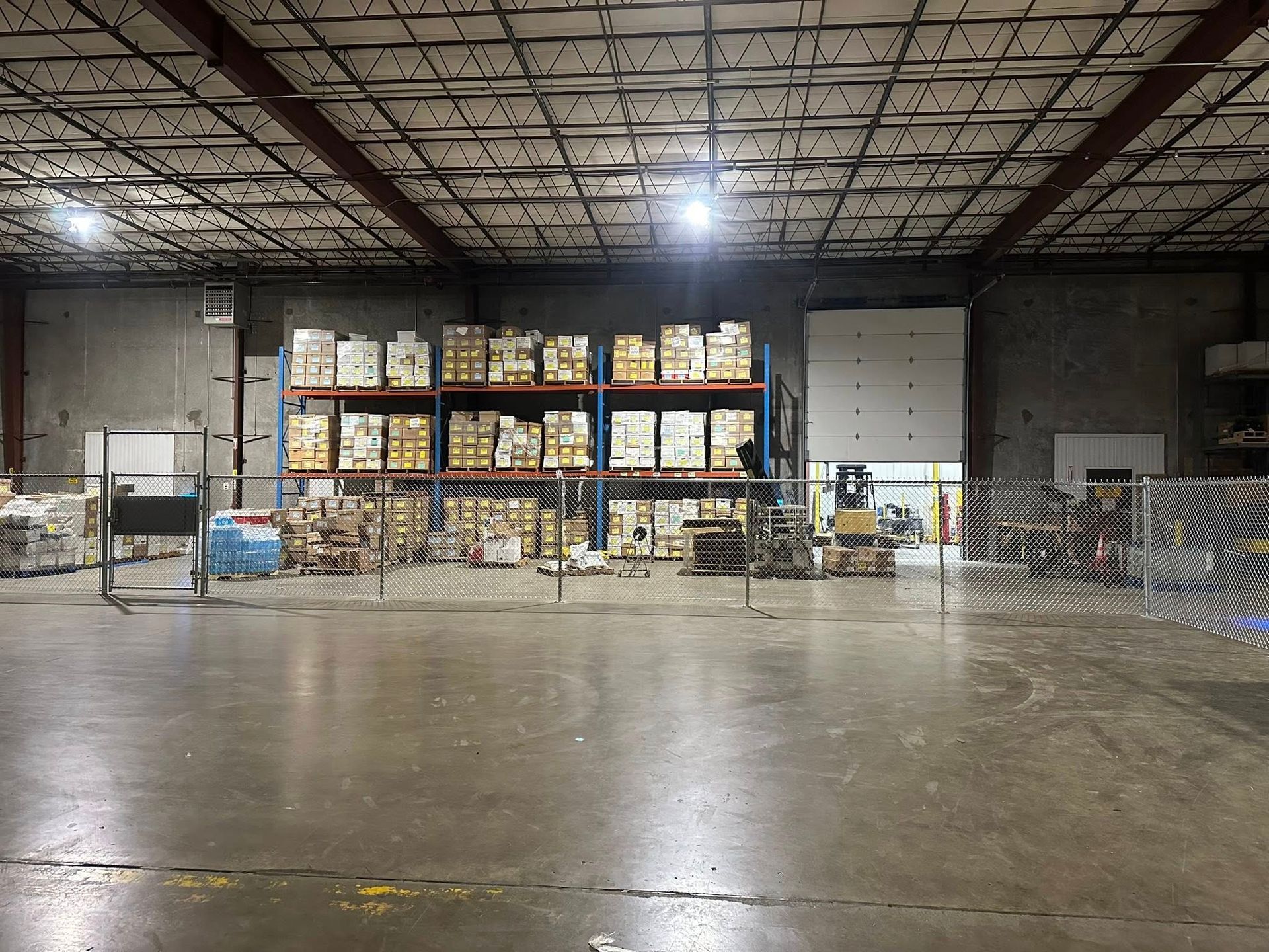 Warehouse interior with stacked pallets of boxes and shelves under bright overhead lights
