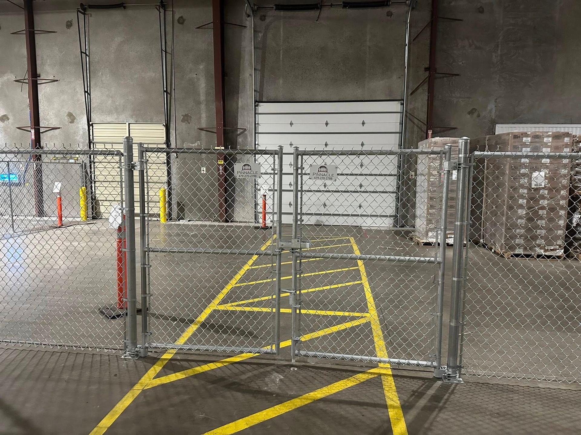 Chain-link gate blocking a yellow-striped loading dock in an industrial warehouse.