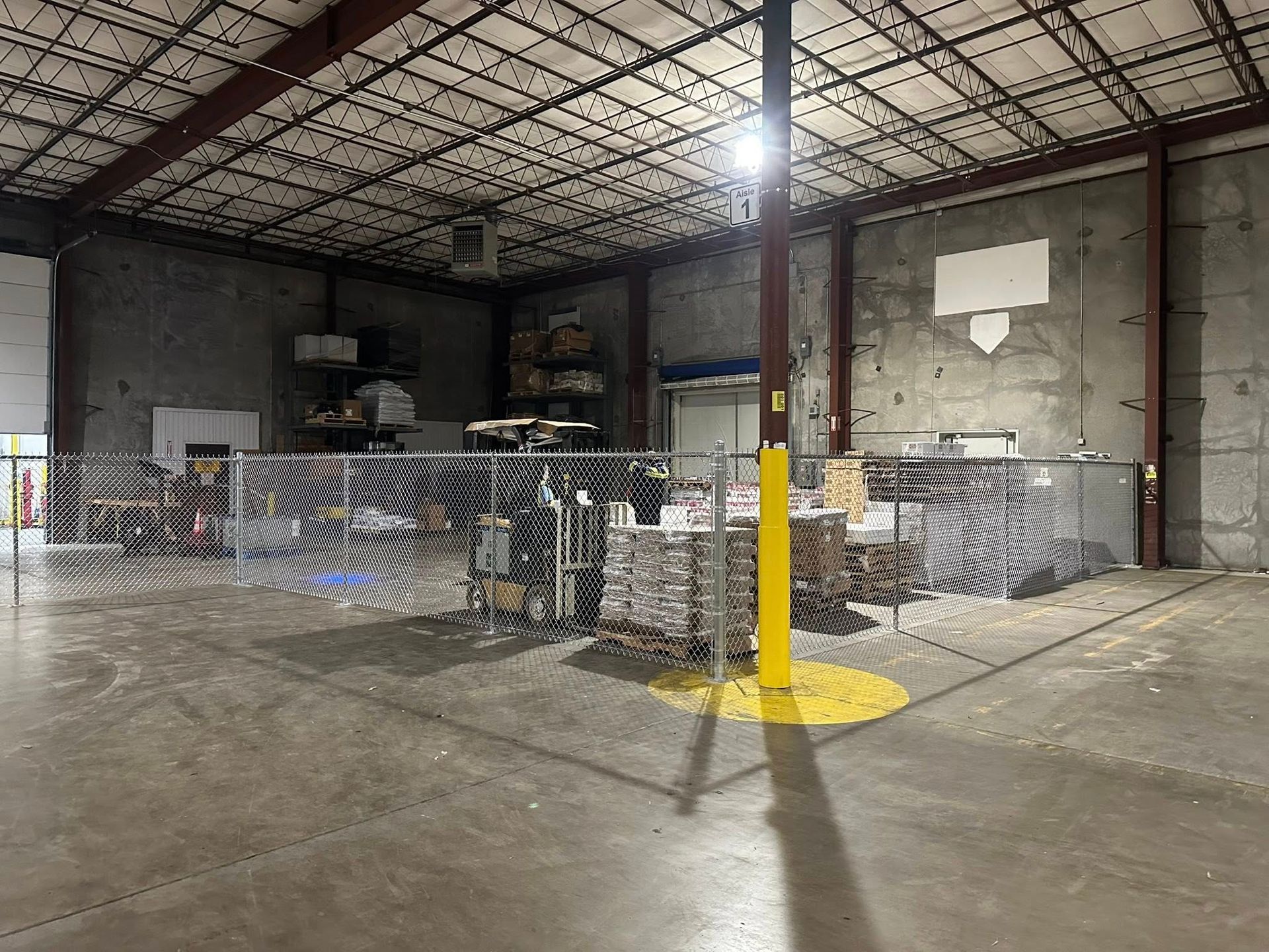 Industrial warehouse interior with stacked wire cages, concrete floor, and a bright overhead light