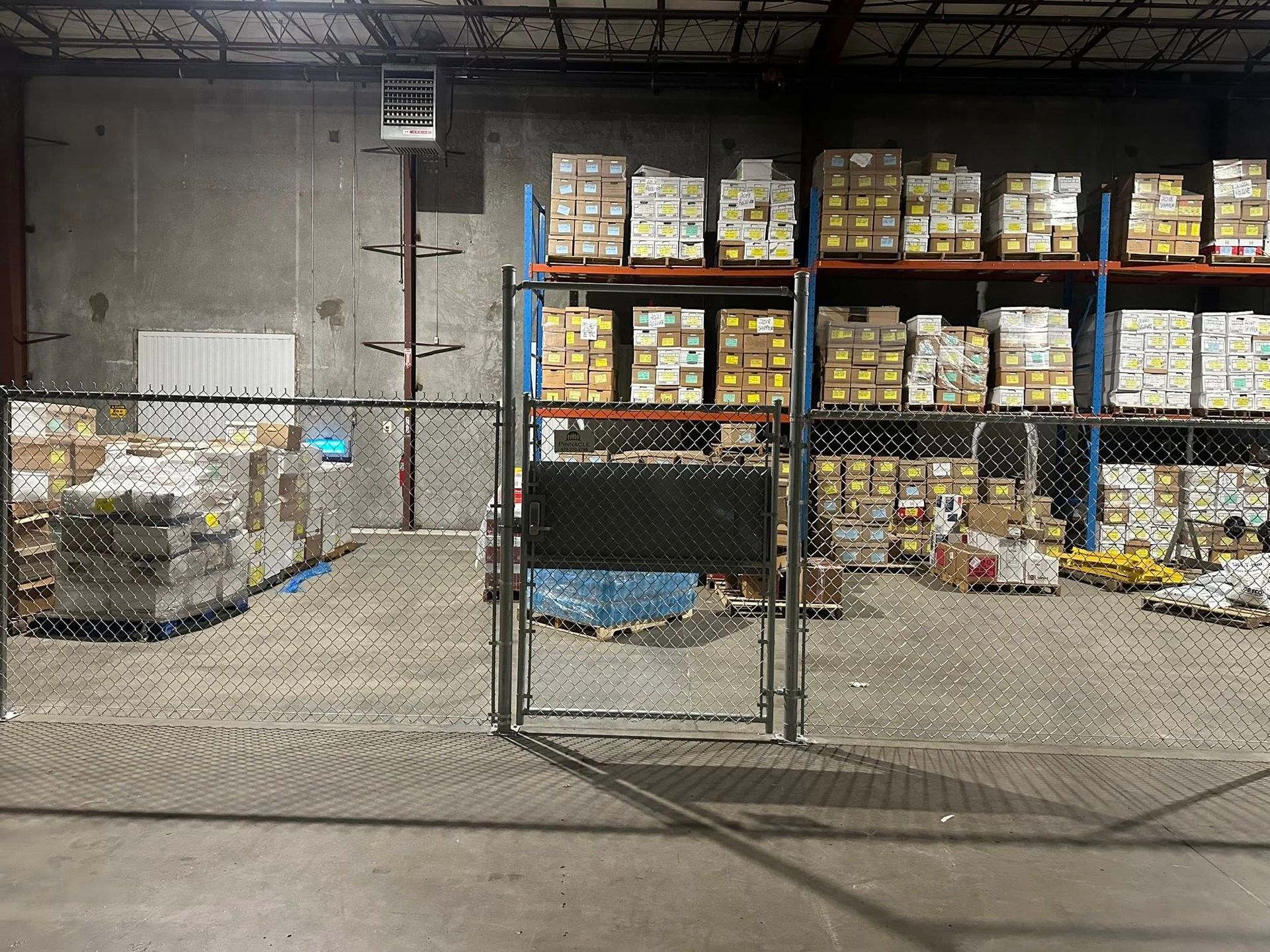 Warehouse storage area with stacked boxes on shelves behind a chain-link fence gate