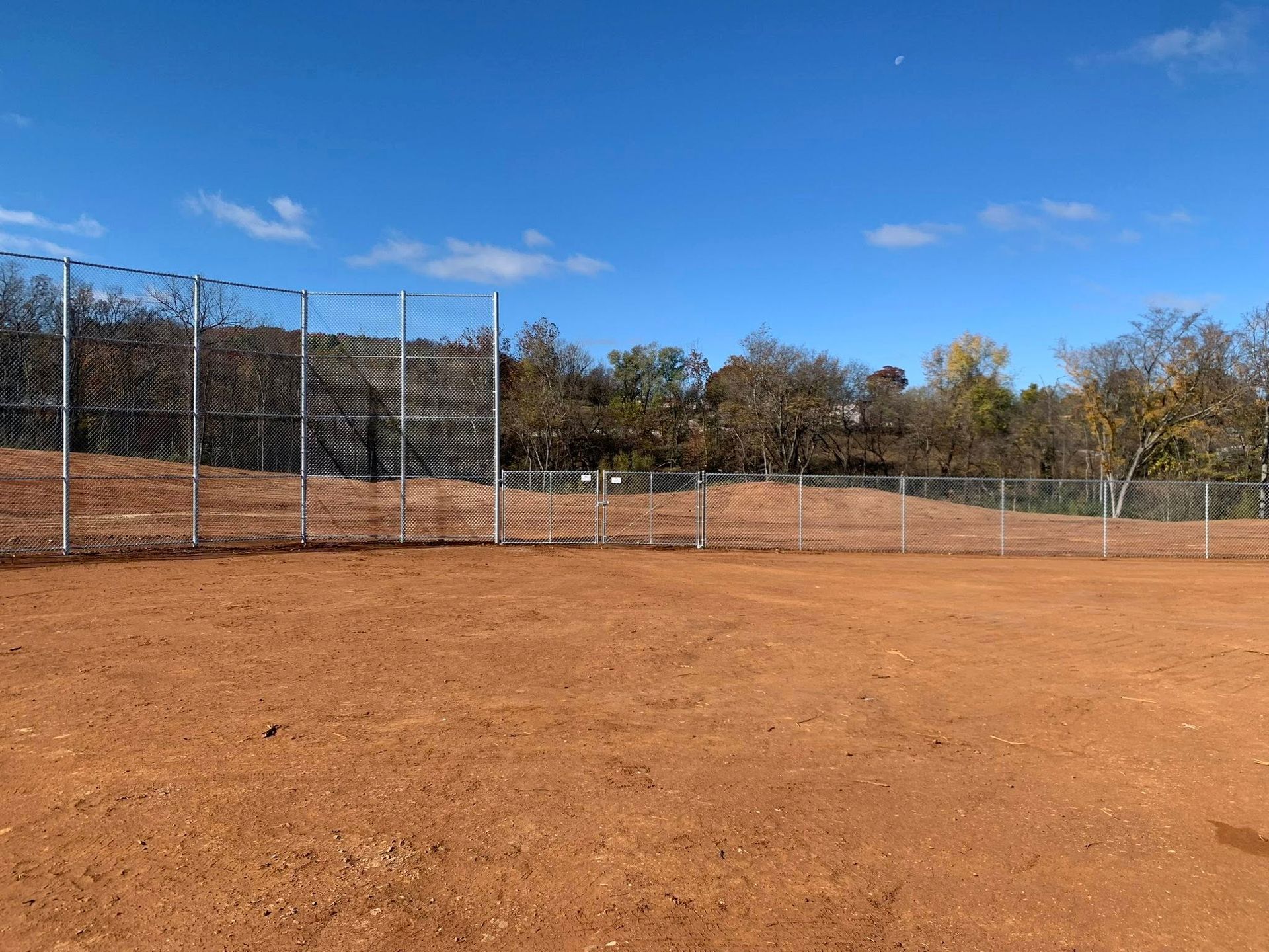 Empty dirt sports field with chain-link fence under a blue sky