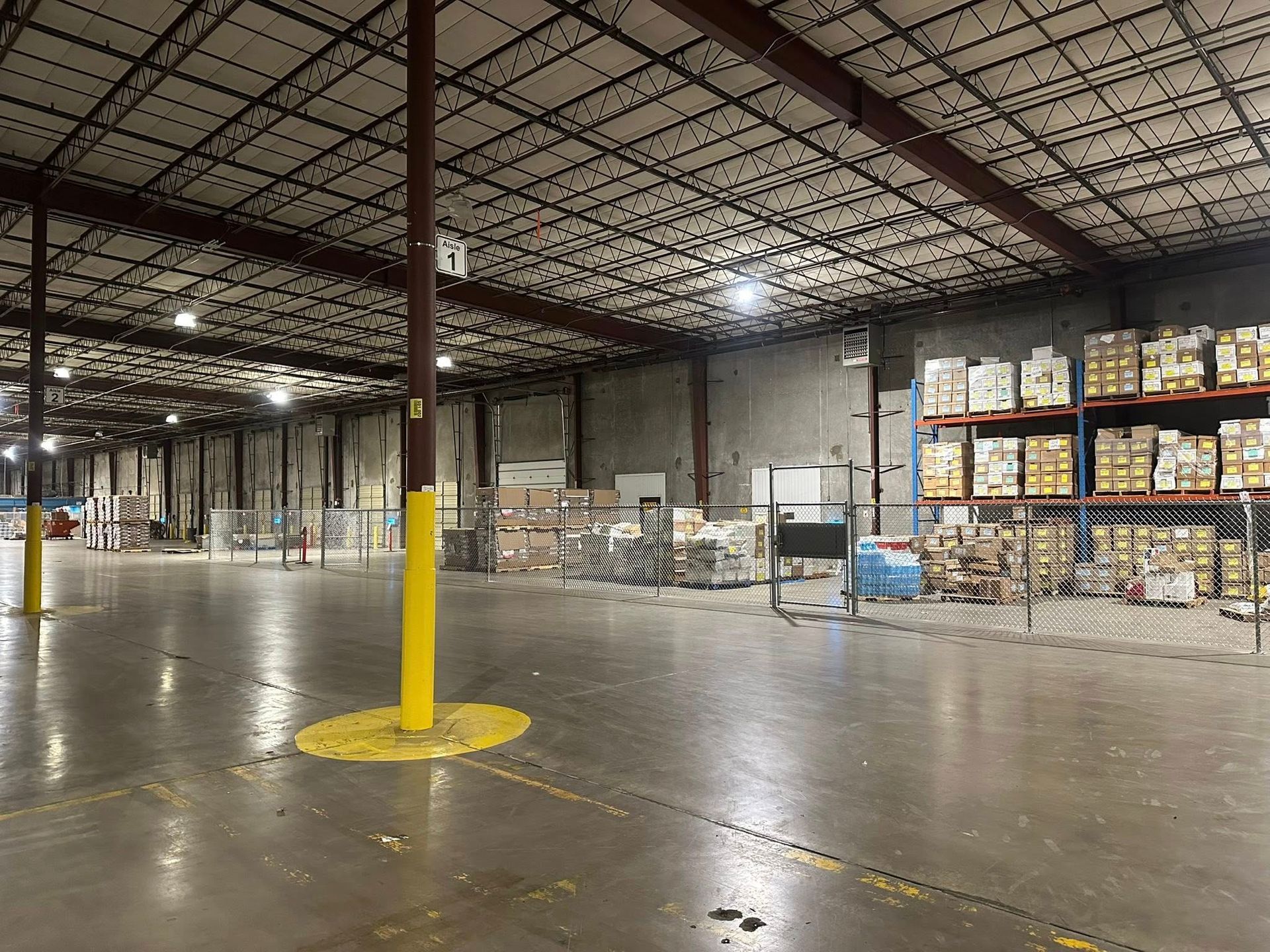 Empty warehouse aisle with stacked pallets, yellow safety post, and polished concrete floor