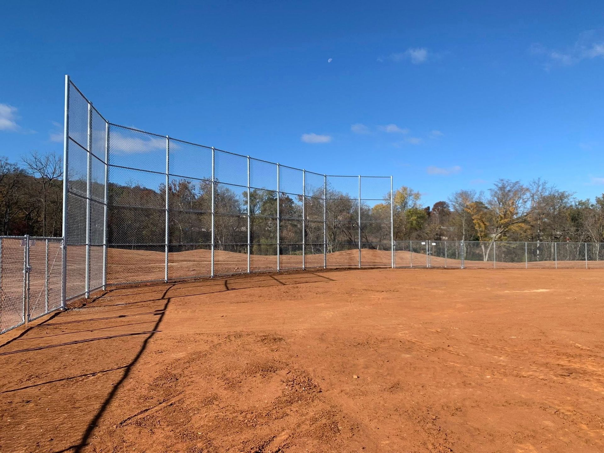 Clay baseball field with a tall chain-link fence and blue sky