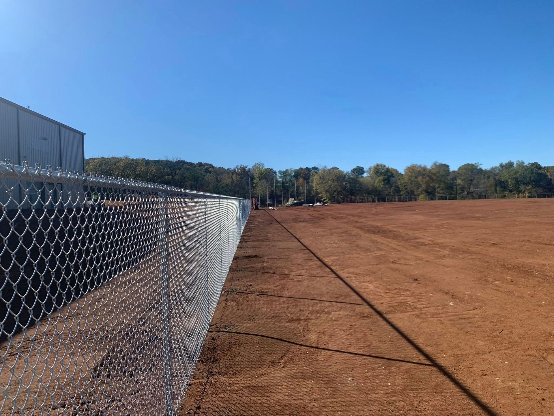 Chain-link fence beside a dirt field under a clear blue sky