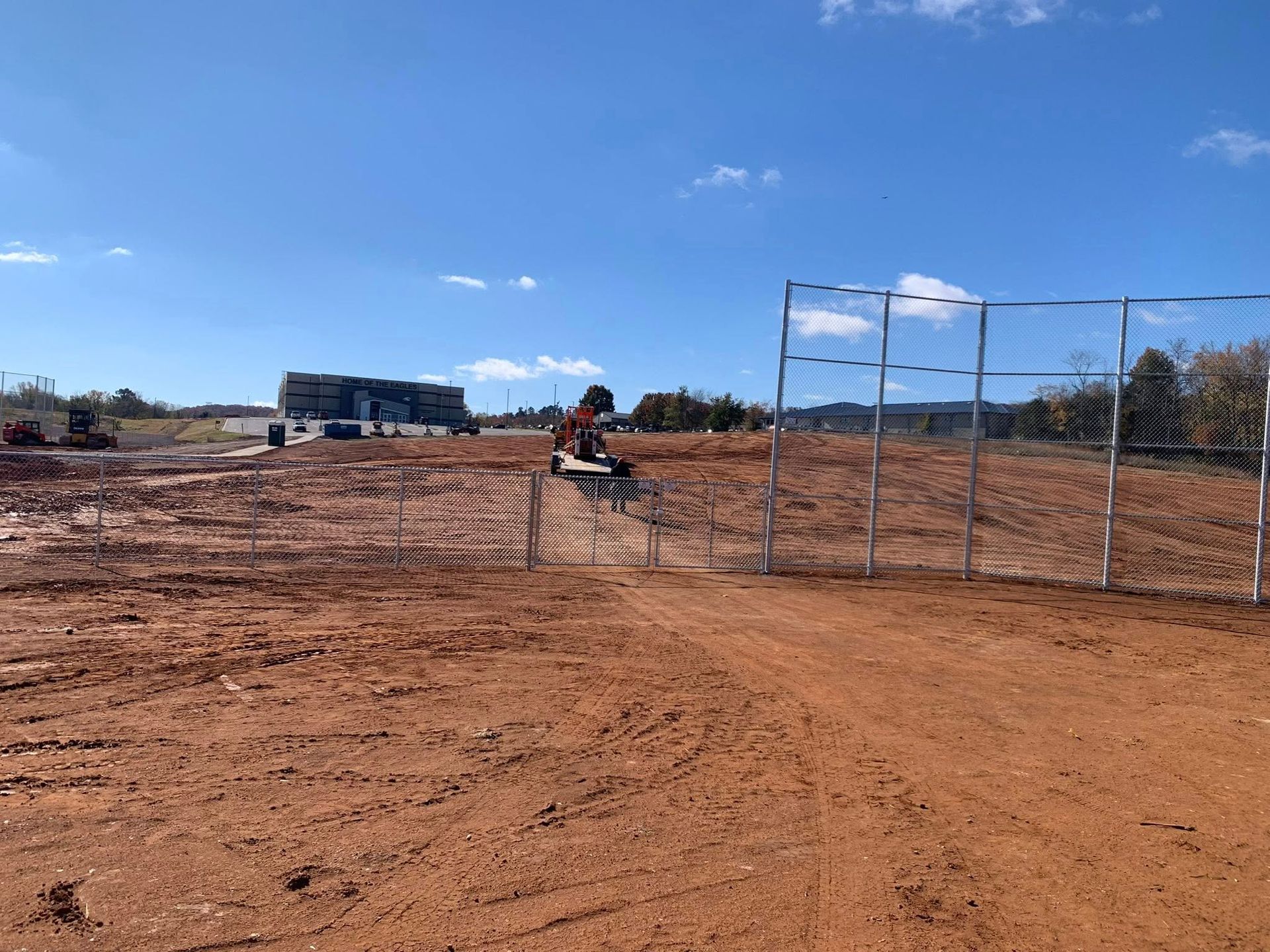 Dirt field with a fenced gate, a person riding an orange ATV, and a building under a blue sky.