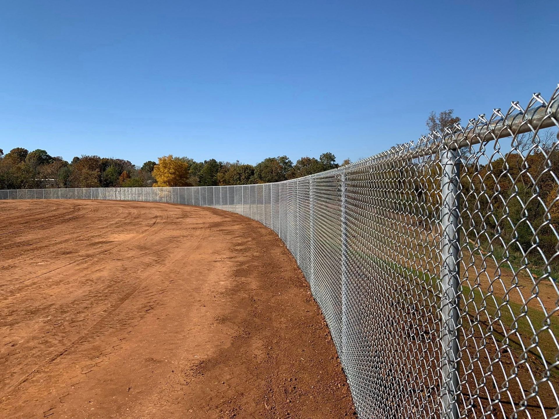 Chain-link fence bordering a dirt path under a clear blue sky