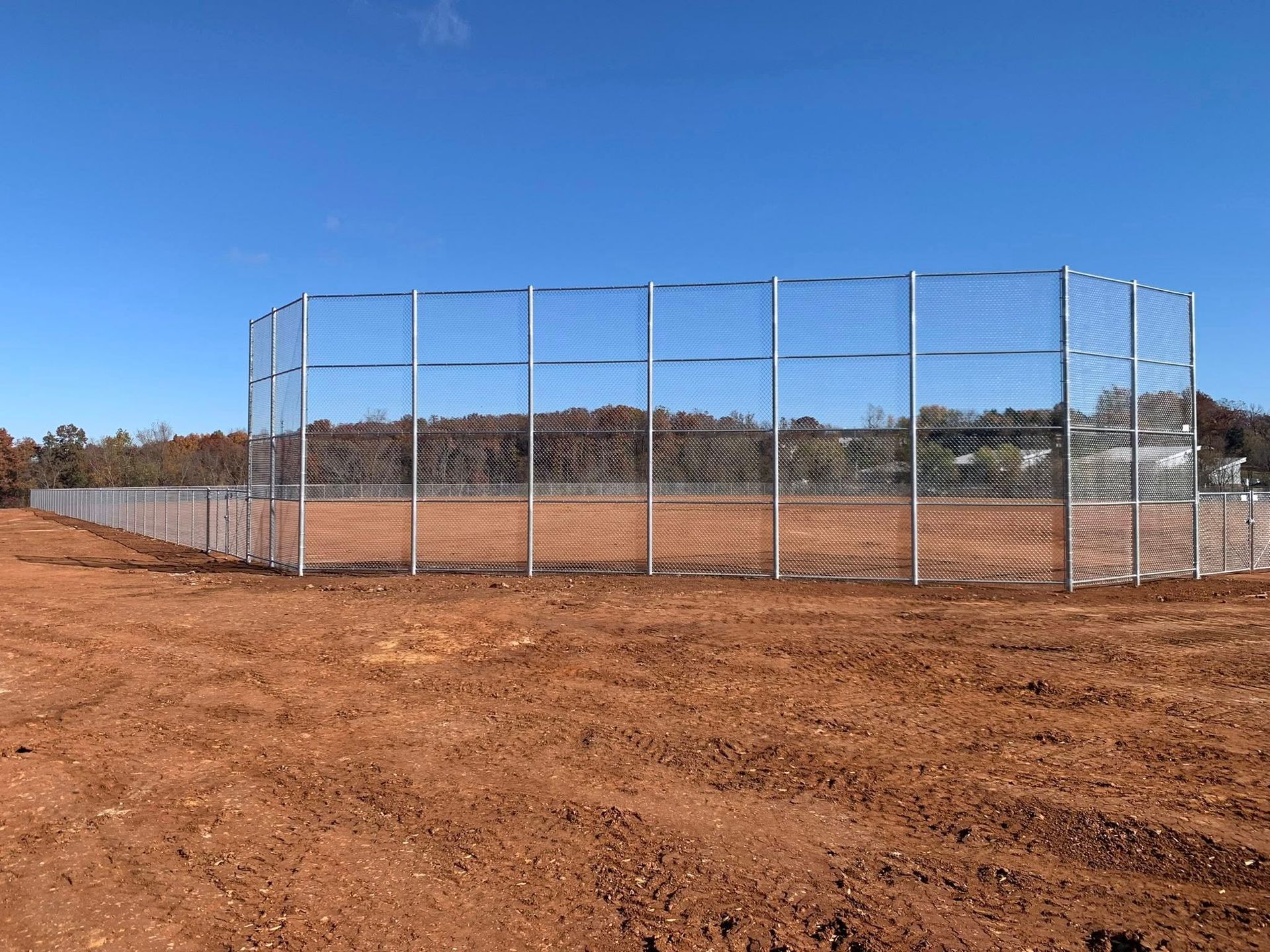 Chain-link baseball field fence on a dirt field under a clear blue sky.
