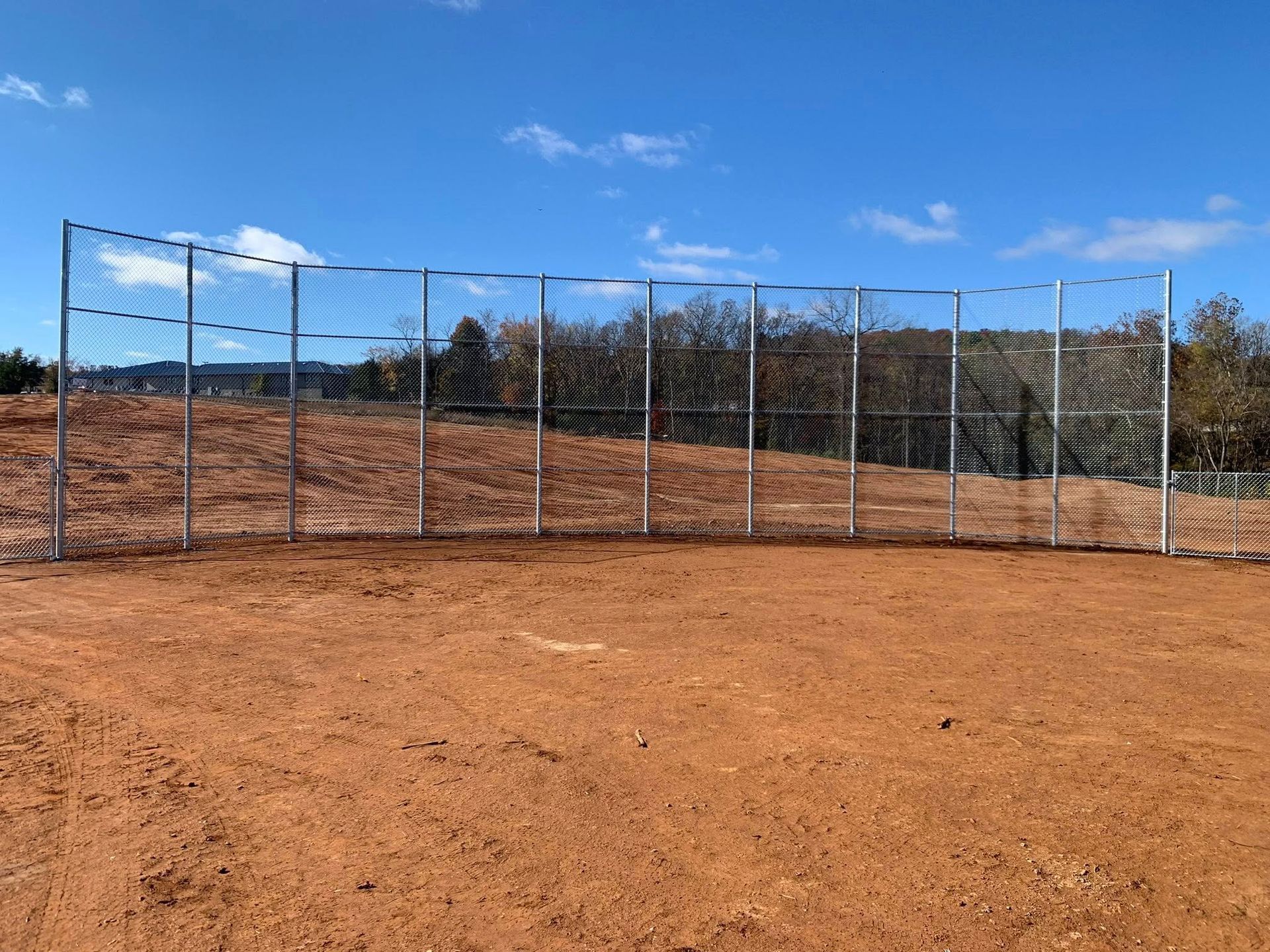Chain-link fence on a dusty sports field under a blue sky with hills in the background